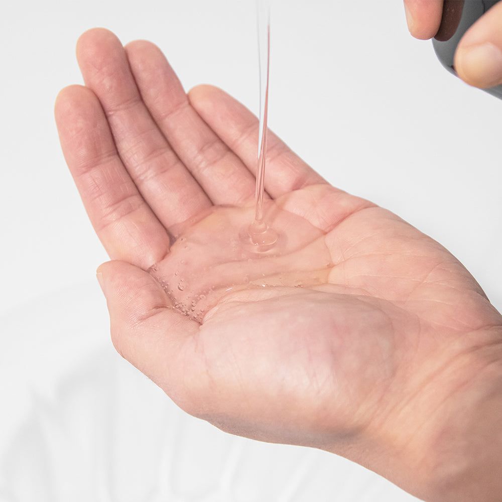 Mano con liquido shampoo. Liquido trasparente versato nella mano. Ambiente luminoso.