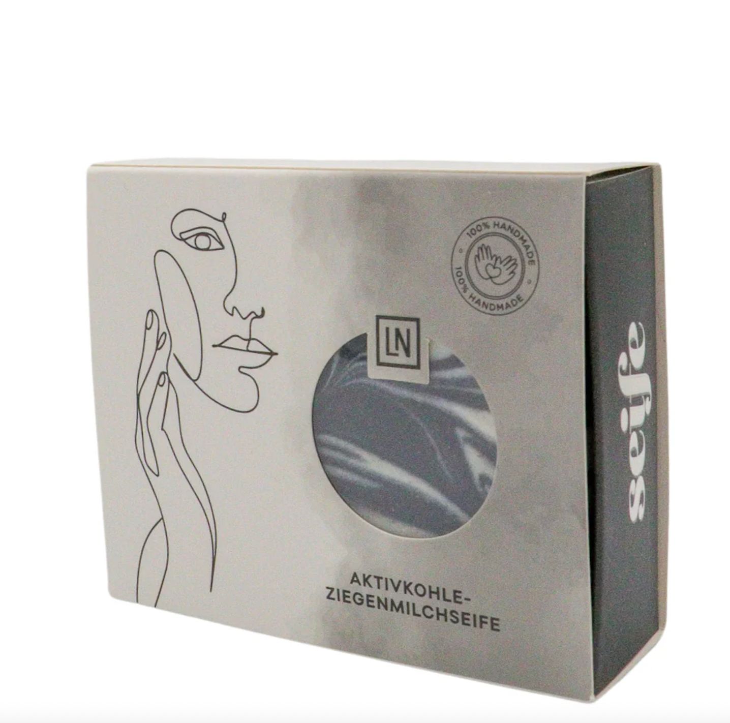 Sapone in scatola. Sapone nero con vortici bianchi visibili attraverso una finestra. Scritta: Aktivkohle-Ziegenmilchseife.
