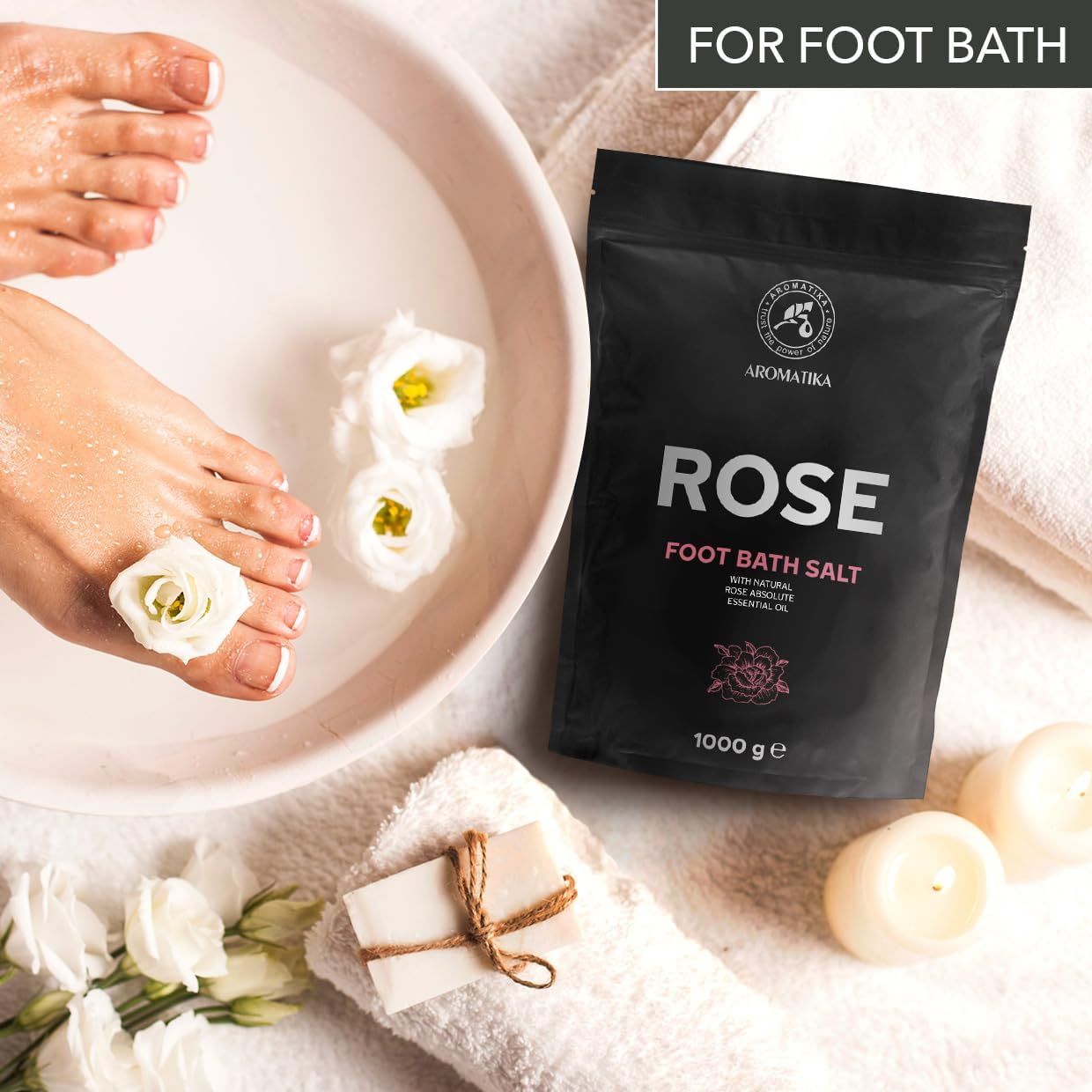 Piedi in una ciotola con sali da bagno Rose. Sacchetto nero, logo Aromatica, 1000 g. Asciugamano, sapone, candele, fiori.