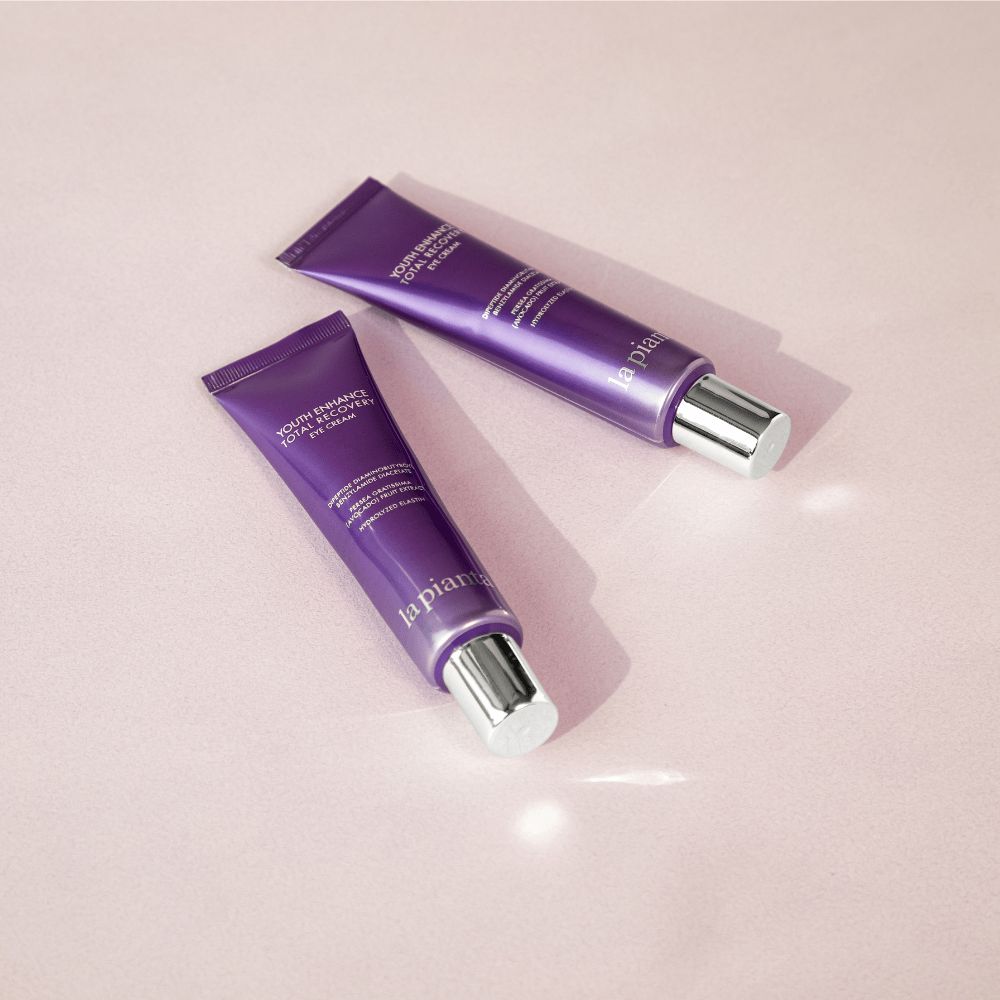 Due tubi viola con tappi bianchi. Scritta: YOUTH ENHANCE TOTAL RECOVERY EYE CREAM, la pianta.