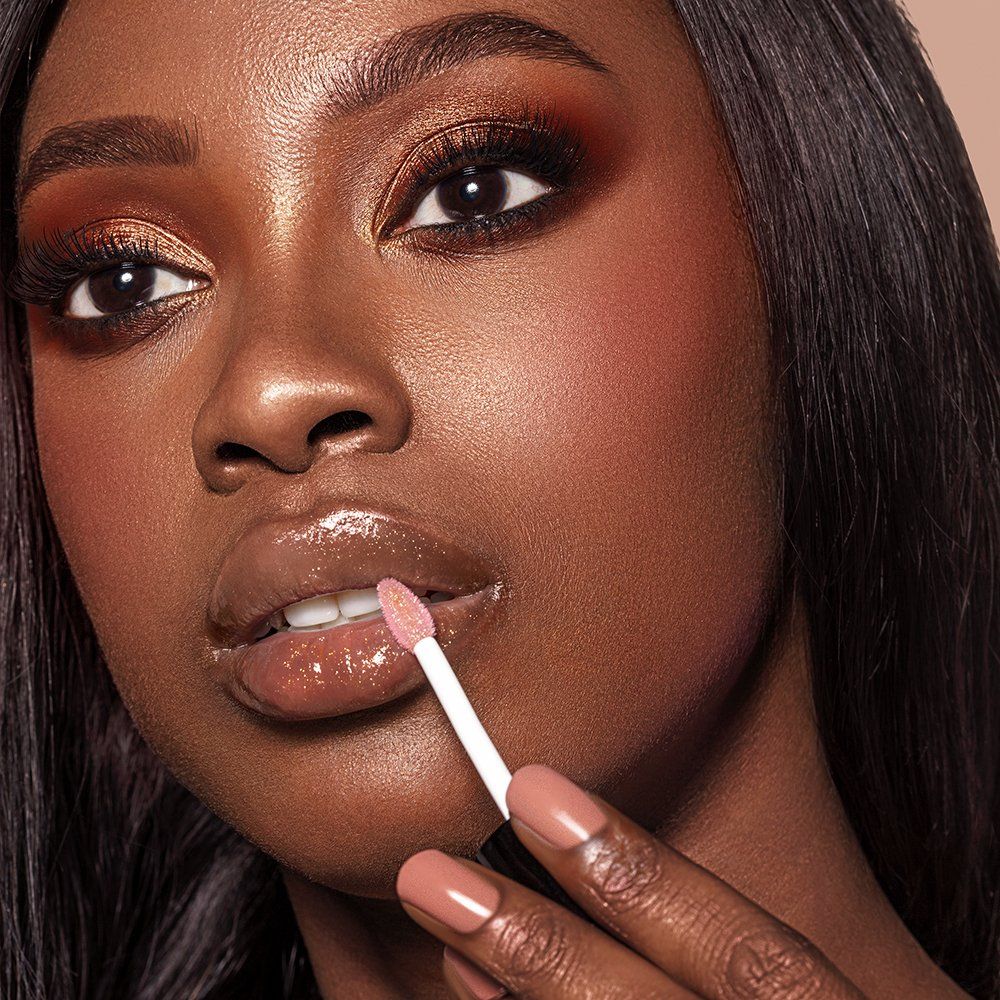Primo piano di una donna che applica l'olio per labbra con un applicatore. Tono della pelle: scuro.