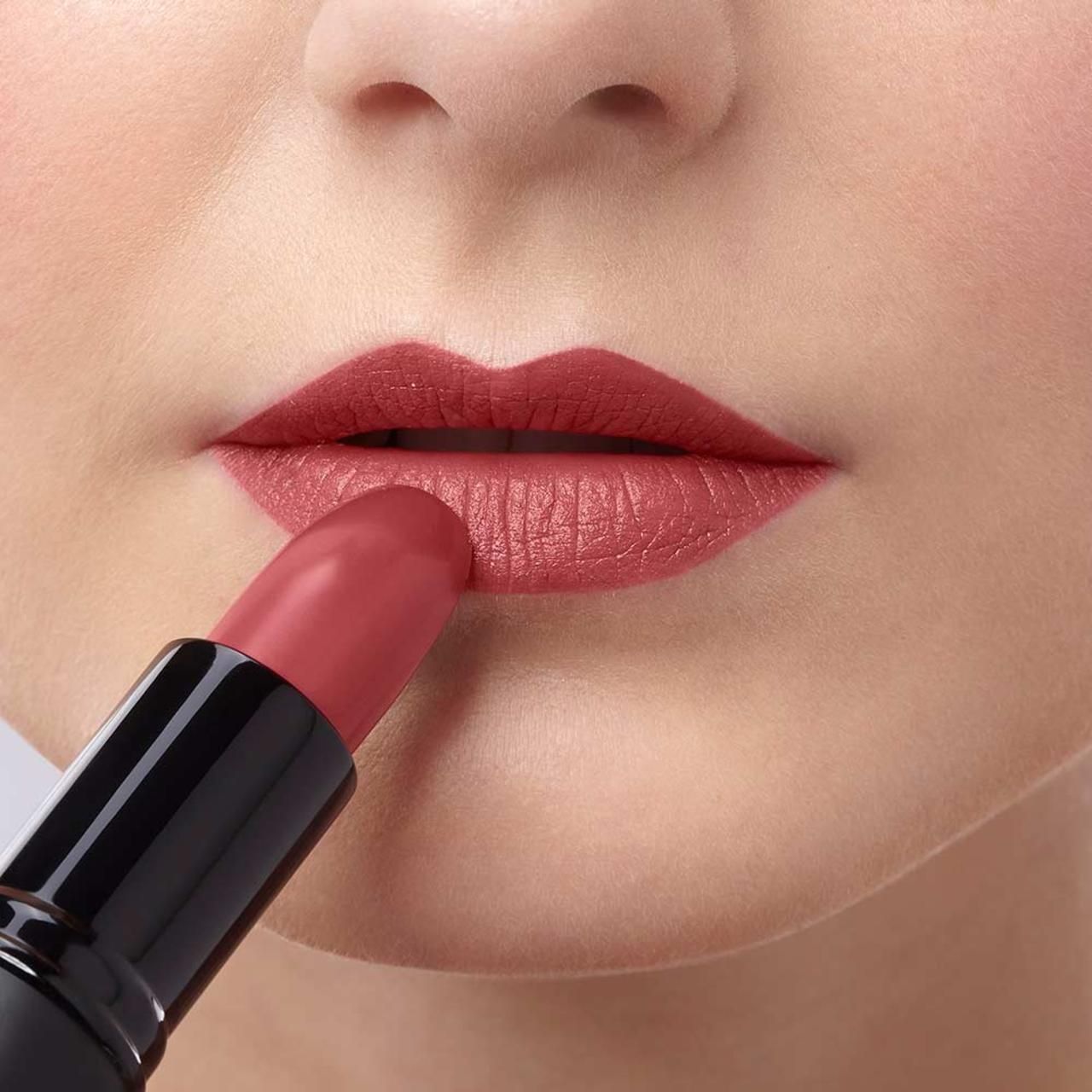 Applicazione di rossetto sulle labbra. Rossetto rosso in astuccio nero. Parte di pelle con labbra e rossetto.