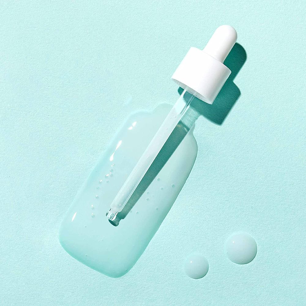 Flacone di vetro con pipetta, siero. Siero e gocce azzurre su sfondo azzurro chiaro. Pipetta con tappo bianco.