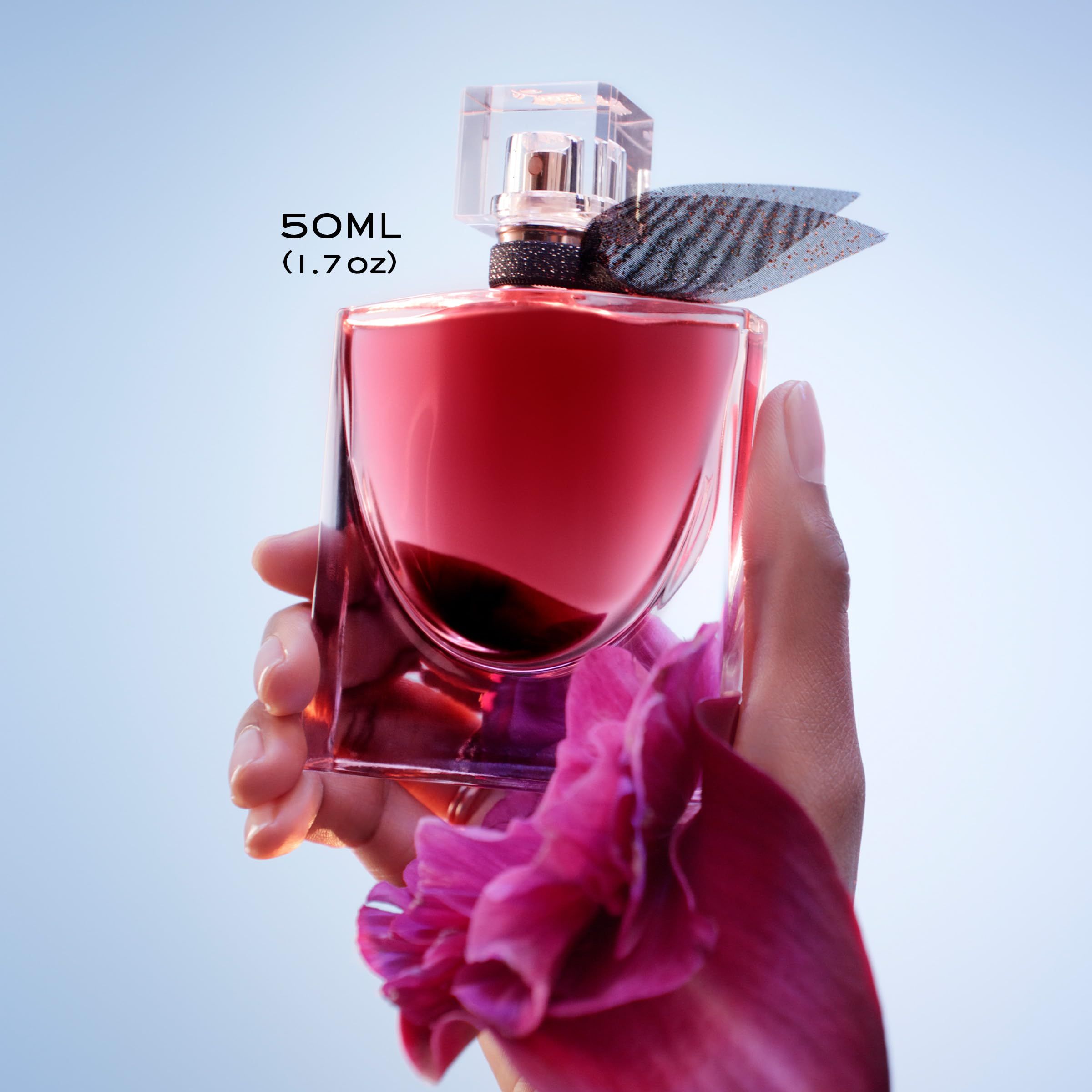 Flacone in vetro con liquido rosso, fiocco nero e tappo trasparente. Etichetta 50ml. Tenuto in mano.