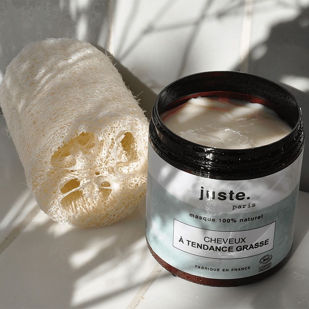 Un barattolo di crema bianca e una spugna di luffa sono posati uno accanto all'altro.