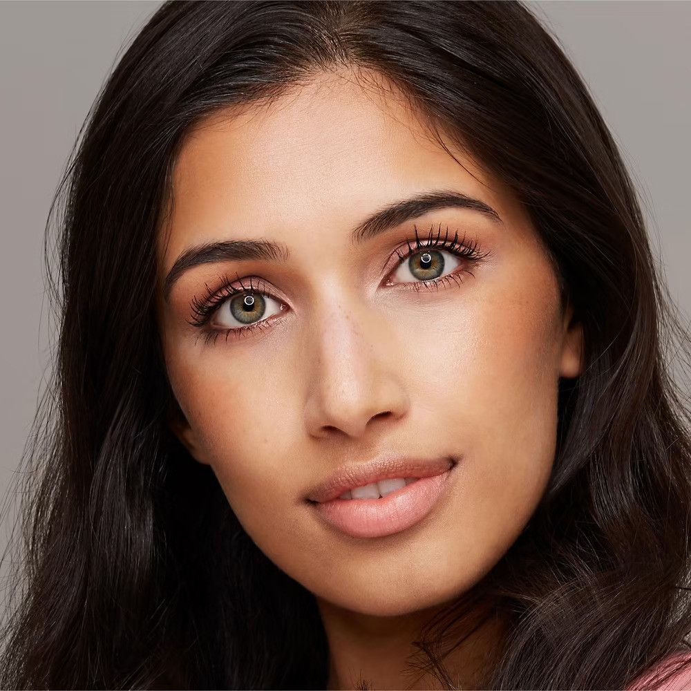 Primo piano di una donna con capelli scuri. Ha gli occhi verdi e indossa il mascara. Guarda la fotocamera.