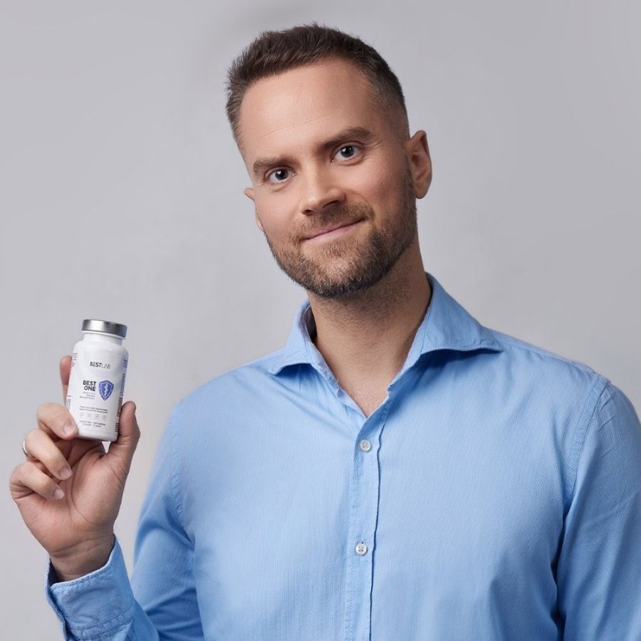 Uomo tiene piccolo flacone bianco. Scritta: BEST LAB BEST ONE. Contiene vitamine D, K, magnesio. 60 capsule.
