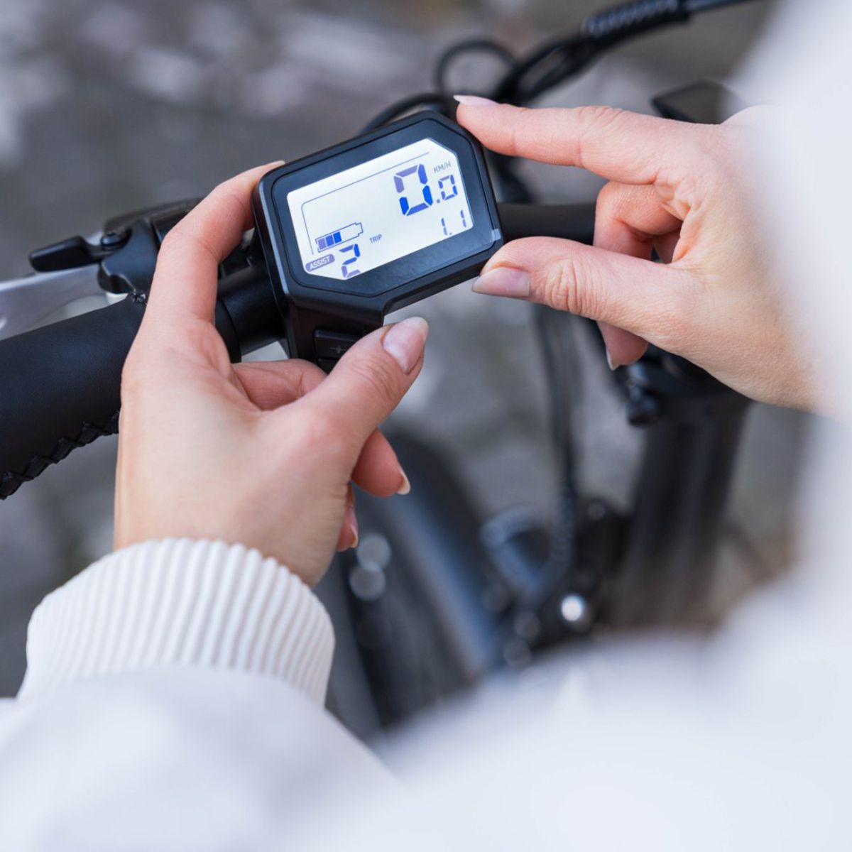 Mani che tengono un display. Cornice nera, schermo bianco con numeri. Visualizzazione della velocità e della batteria.