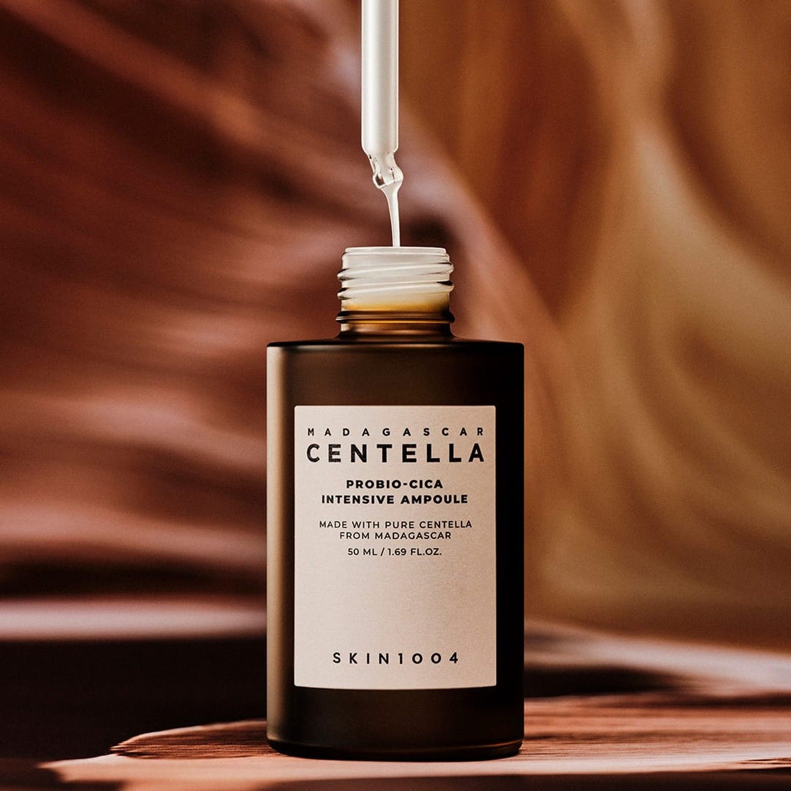 Un contagocce versa il siero in un flacone marrone aperto, etichetta 'Centella Probio-Cica Intensive Ampoule'.