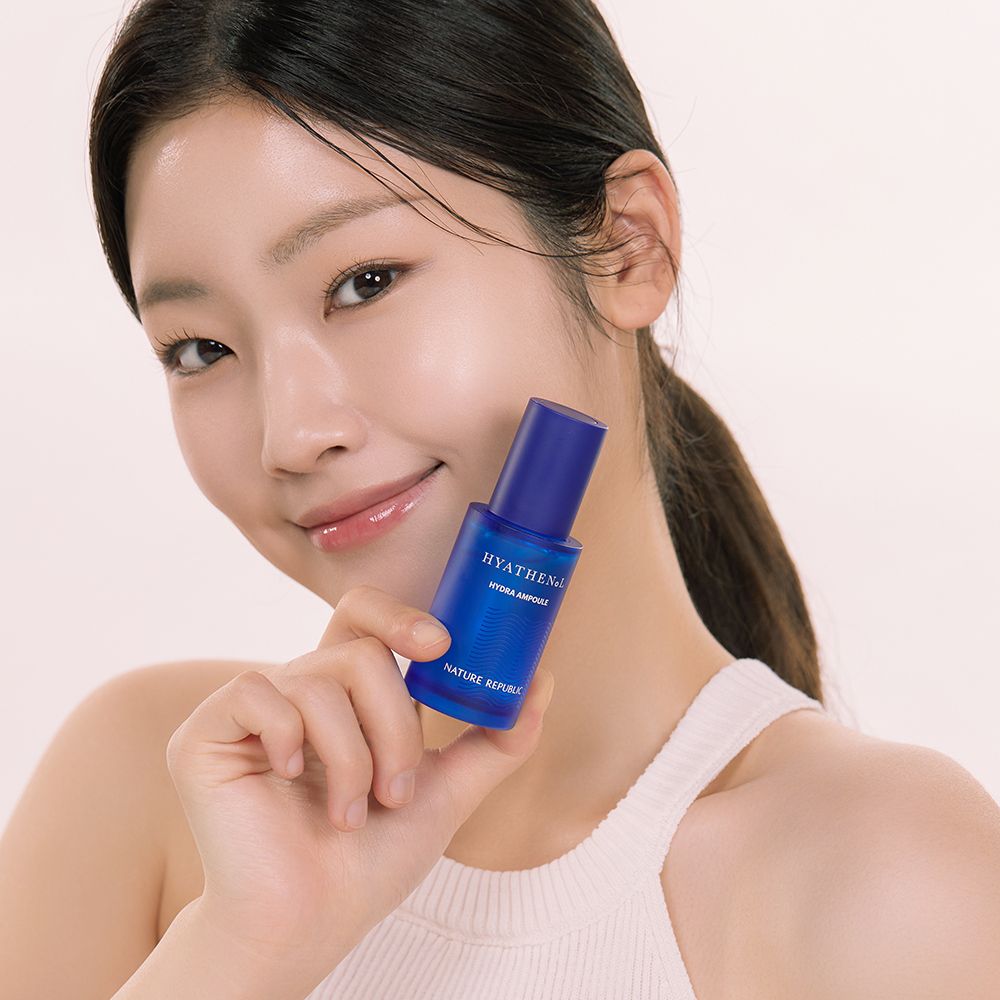 Donna tiene flacone di siero blu. Scritta: HYATHENOL Hydra Ampoule, NATURE REPUBLIC. La donna sorride.