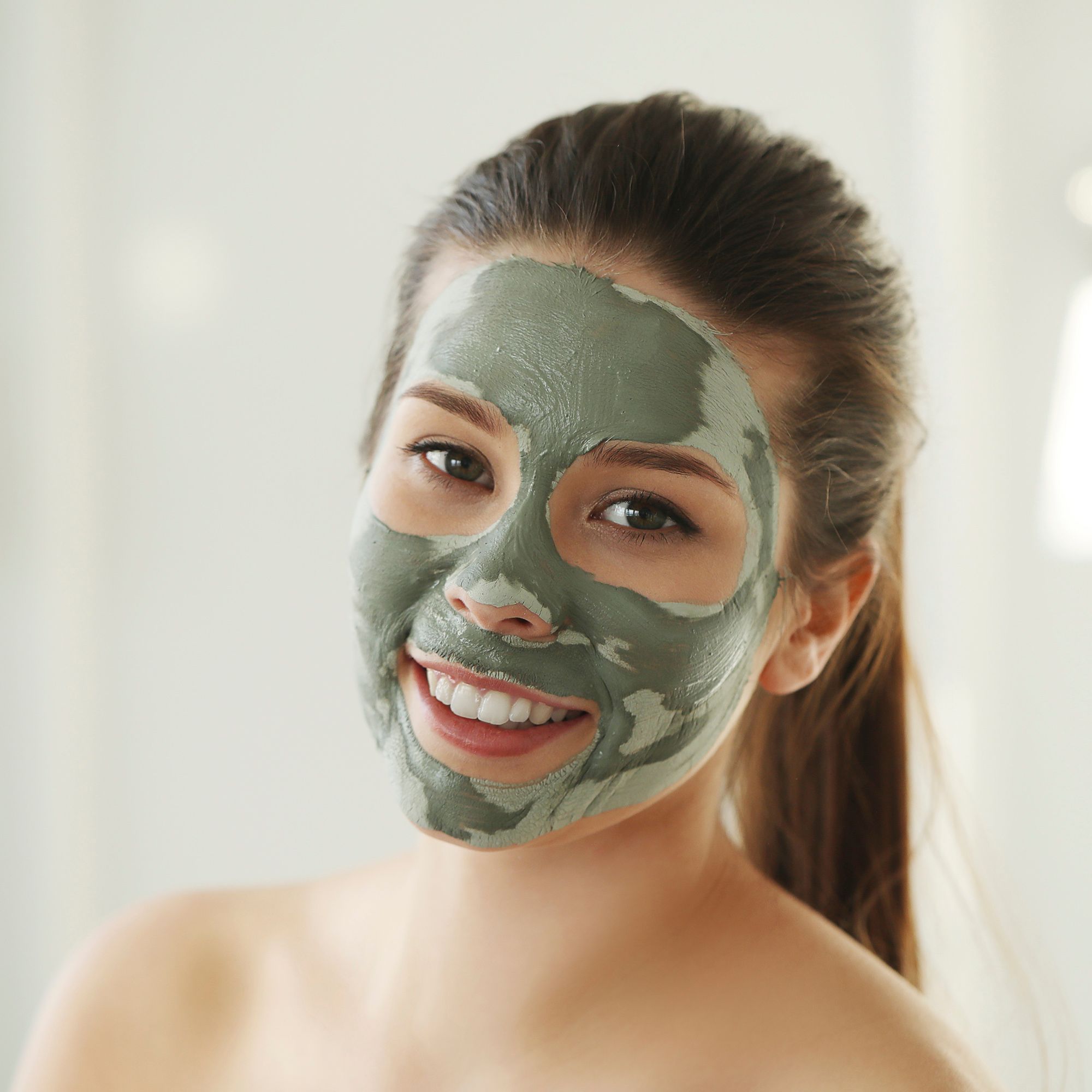 Donna con maschera all'argilla verde sul viso. Sorride.