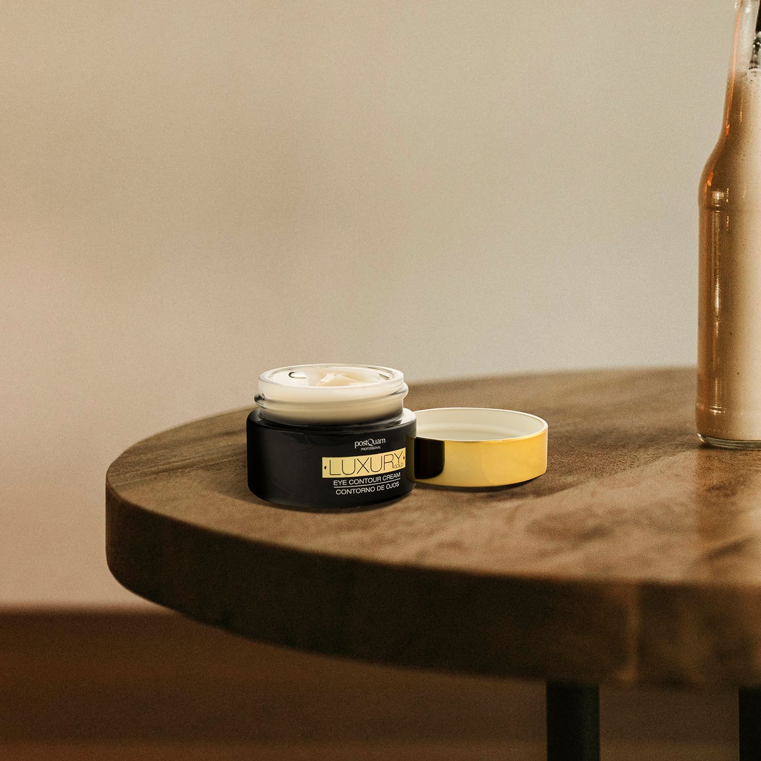 Vasetto aperto su un tavolo. Coperchio dorato accanto. Nome prodotto: LUXURY GOLD EYE CONTOUR CREAM.