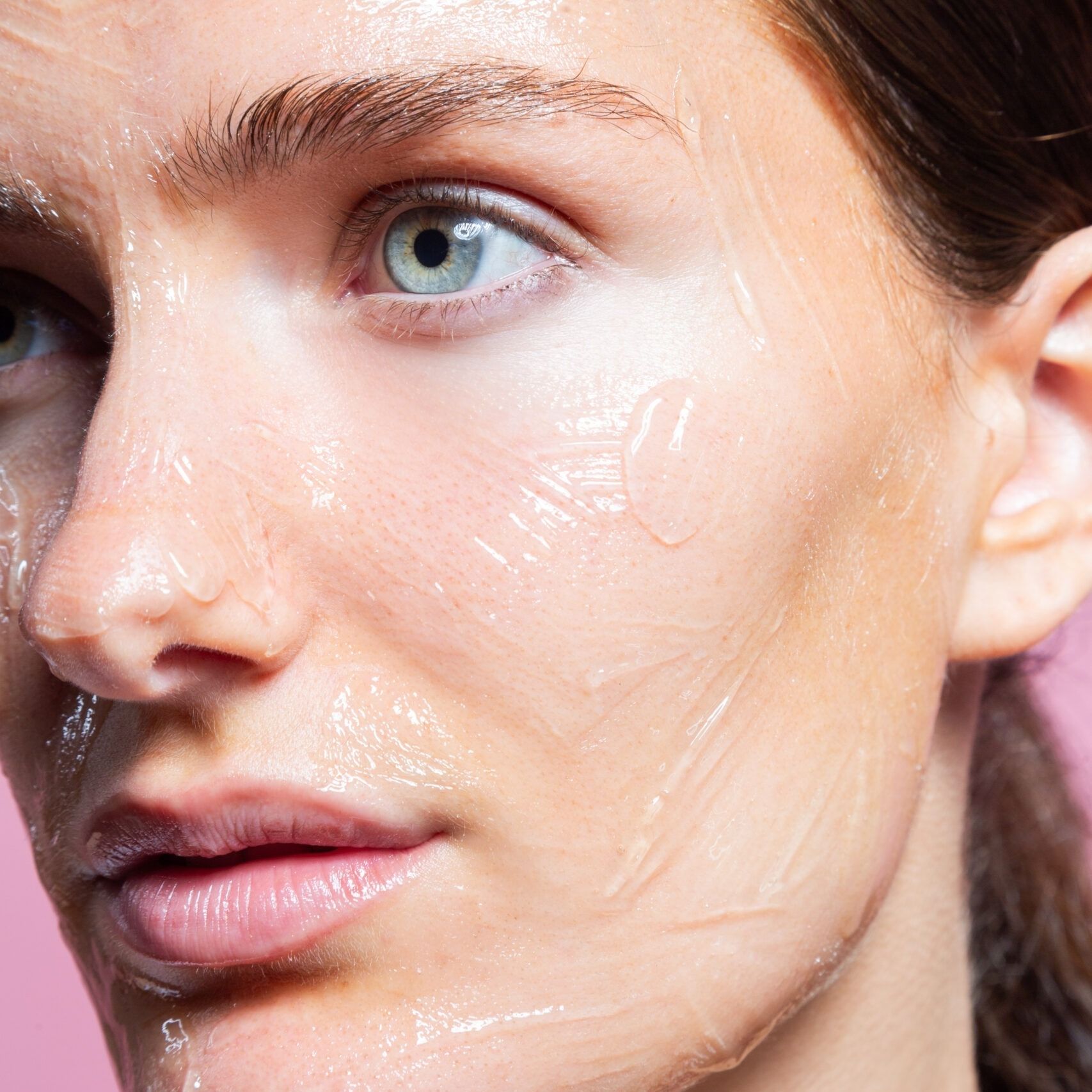 Primo piano di un viso con gel trasparente. Sfondo rosa. Prodotto per la cura della pelle applicato.