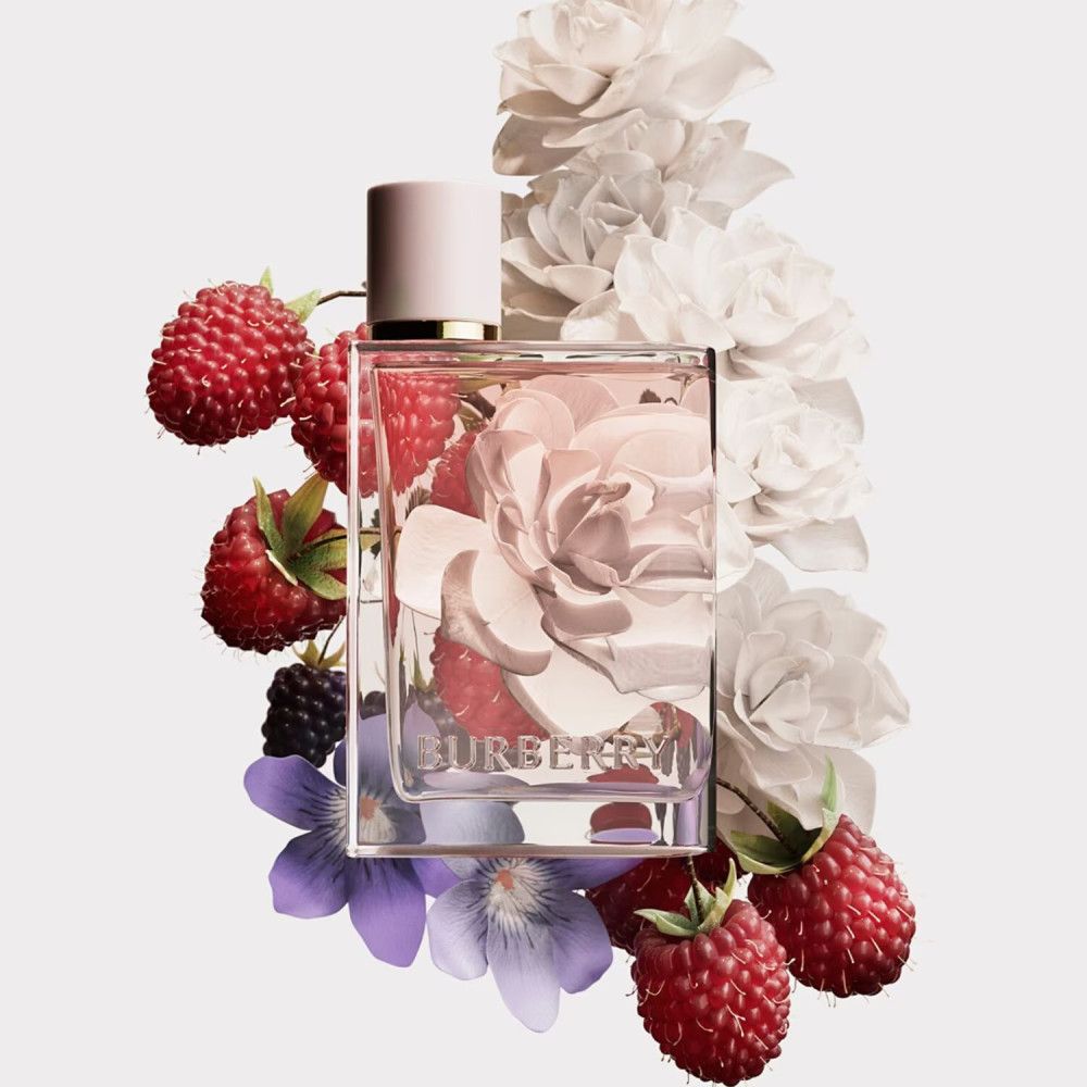 Flacone di Burberry Her Eau de Parfum, circondato da lamponi, more, fiori e petali. Il flacone è quadrato.