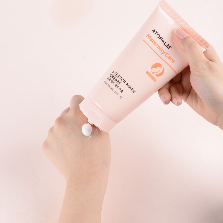 Persona che applica la crema sulla mano. Tubo rosa con testo bianco. Nome prodotto: STRETCH MARK CREAM.