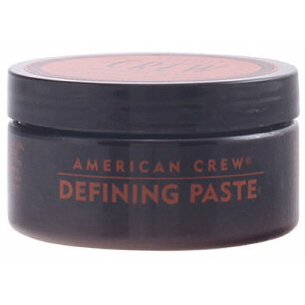 Barattolo cilindrico con corpo e coperchio marrone. "AMERICAN CREW DEFINING PASTE" in marrone. Coperchio nero.