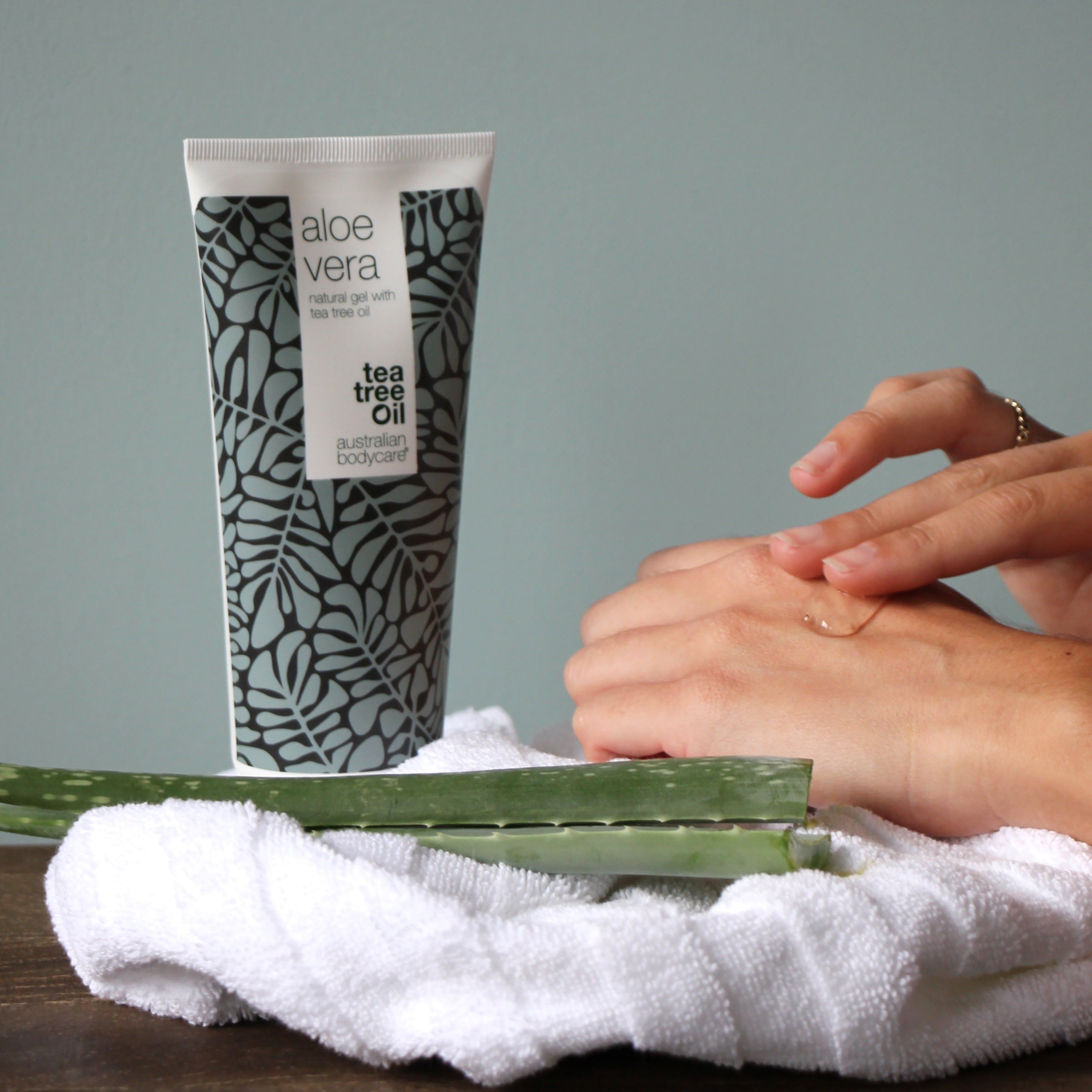 Persona applica gel sulla mano. Tubo di gel all'aloe vera, motivo a foglie grigie. Scritta: Aloe Vera, Tea Tree Oil, Australian Bodycare.