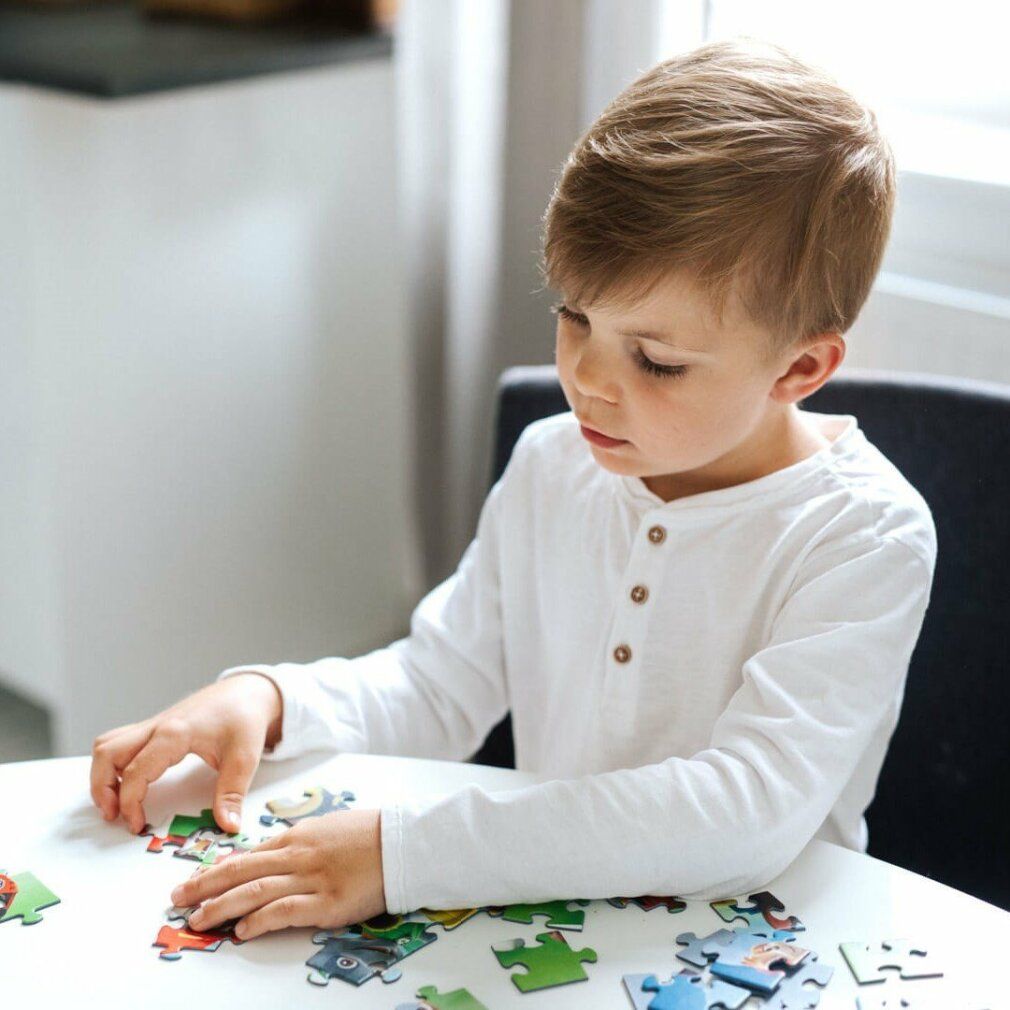 Un bambino è seduto a un tavolo e fa un puzzle. I pezzi del puzzle sono sparsi sul tavolo.
