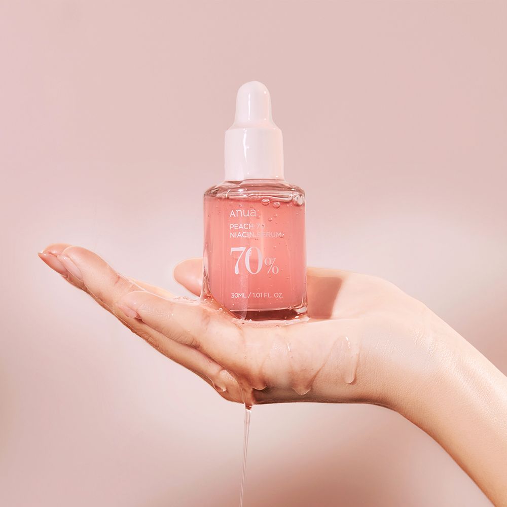 Mano che tiene un flacone di siero Anua Peach 70 Niacin, il siero gocciola.