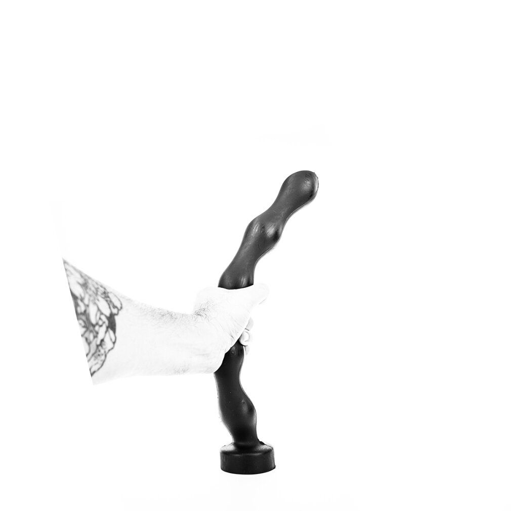 Plug anale nero tenuto da una mano tatuata. Testa sferica, superficie scanalata, base rotonda.