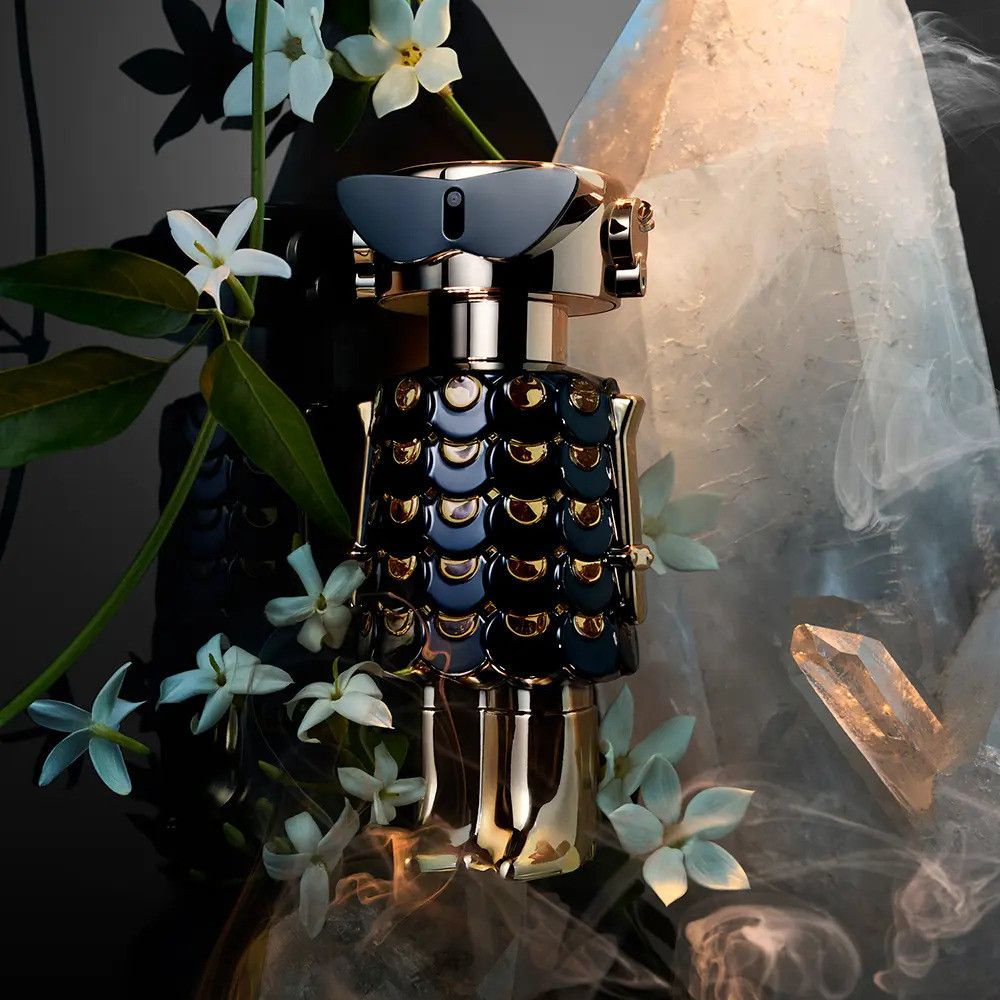 Flacone di profumo nero e oro, circondato da fiori bianchi e cristalli.