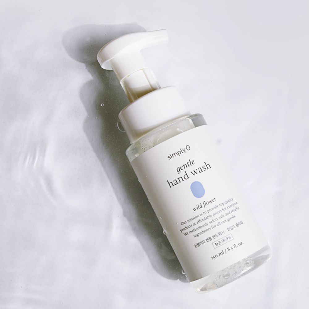 Flacone trasparente con dosatore bianco. Etichetta con nome del prodotto e motivo floreale. Su superficie d'acqua con ombra.
