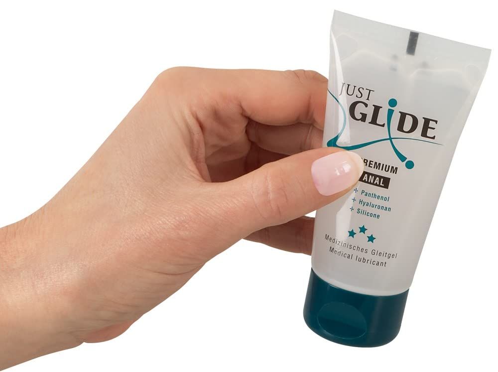 Mano che tiene un tubo di gel lubrificante Just Glide Premium Anal. Contenitore trasparente con tappo blu.