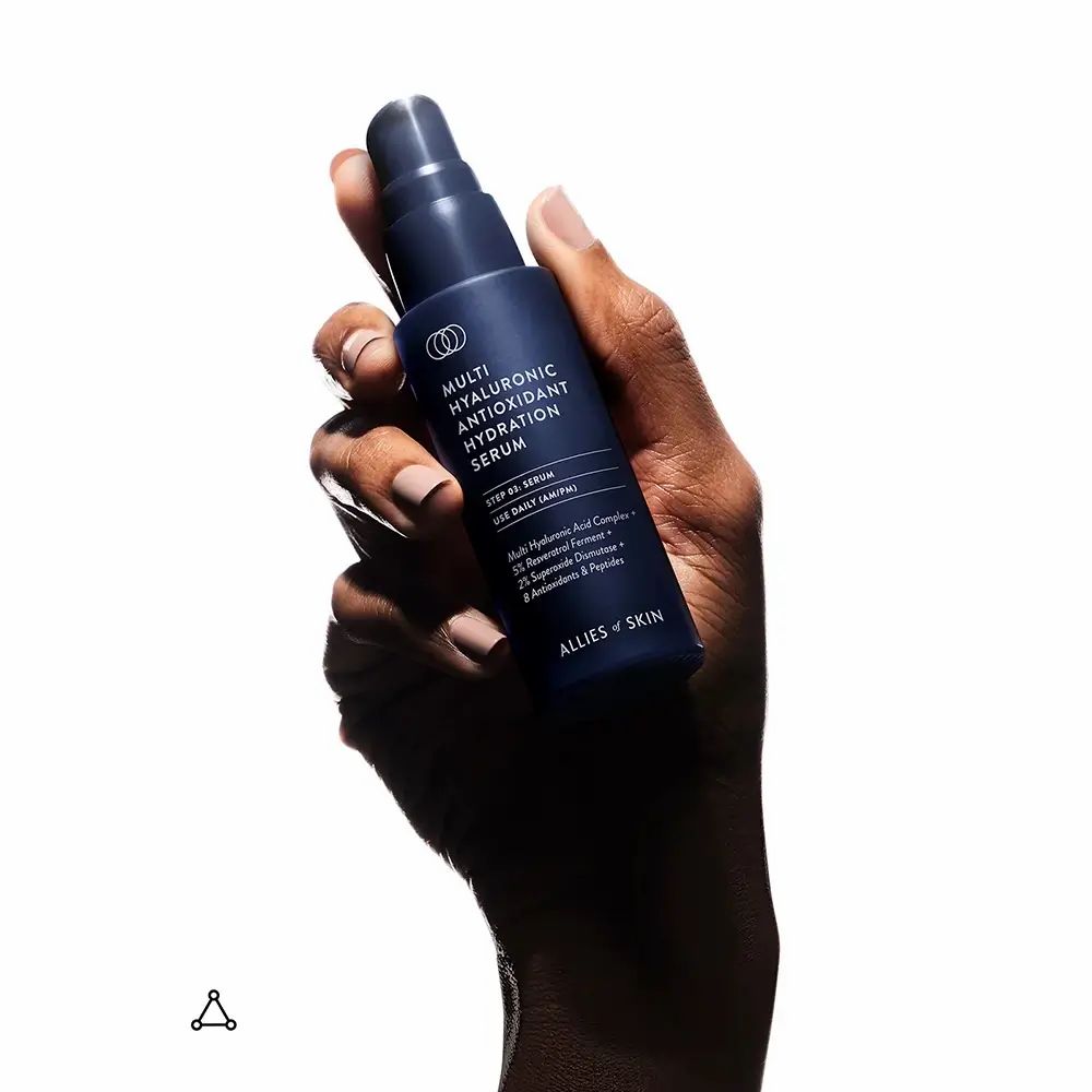 Mano che tiene un flacone di siero. Testo: Multi Hyaluronic Antioxidant Hydration Serum, Allies of Skin.