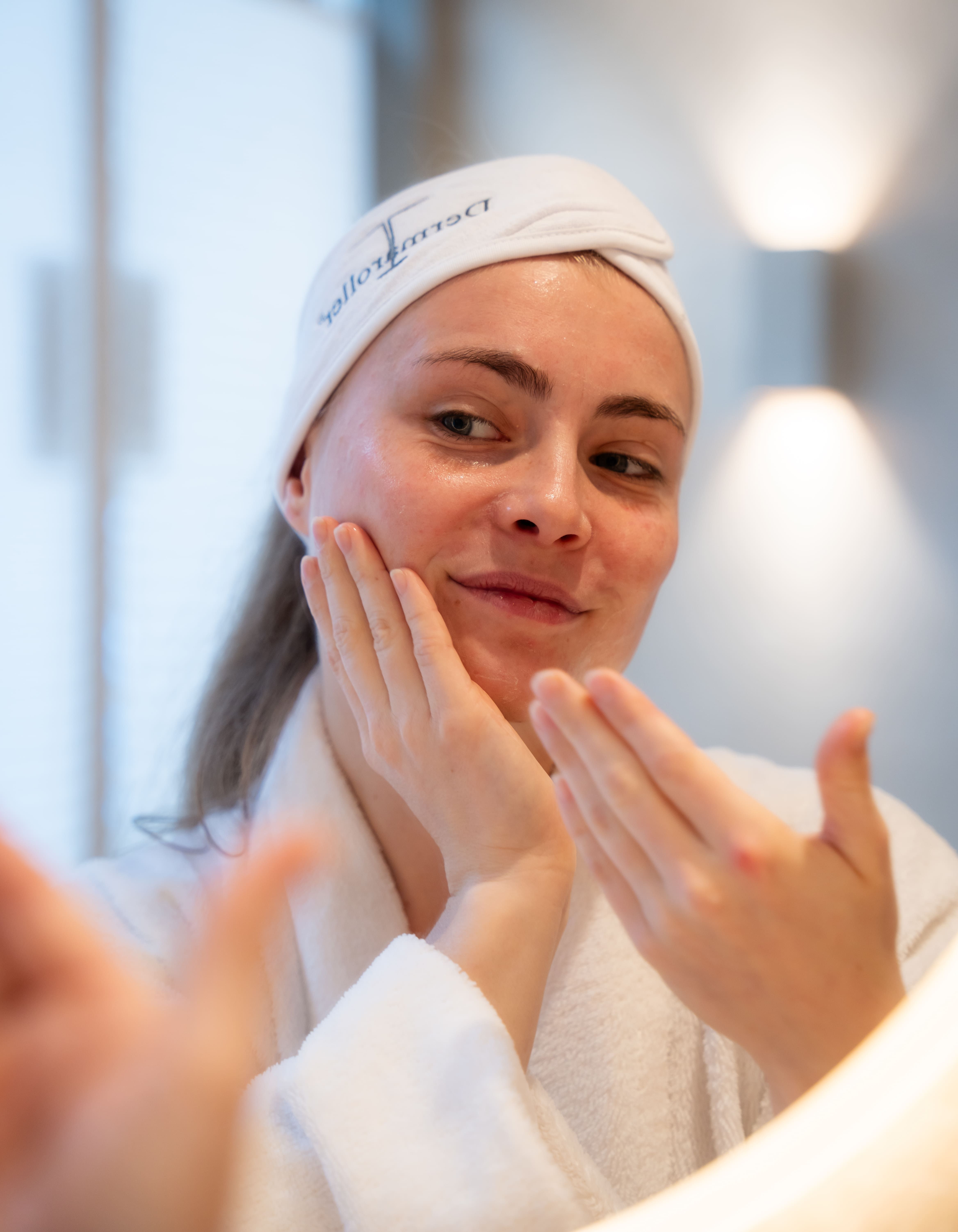 Donna applica il siero Dermaroller Hyal C sul viso, indossa una fascia e un accappatoio.