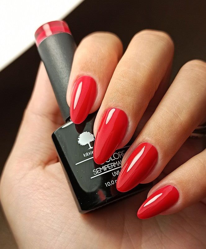 Mani con unghie rosse smaltate. Flacone smalto con scritta: LCI, Colore Semipermanente.