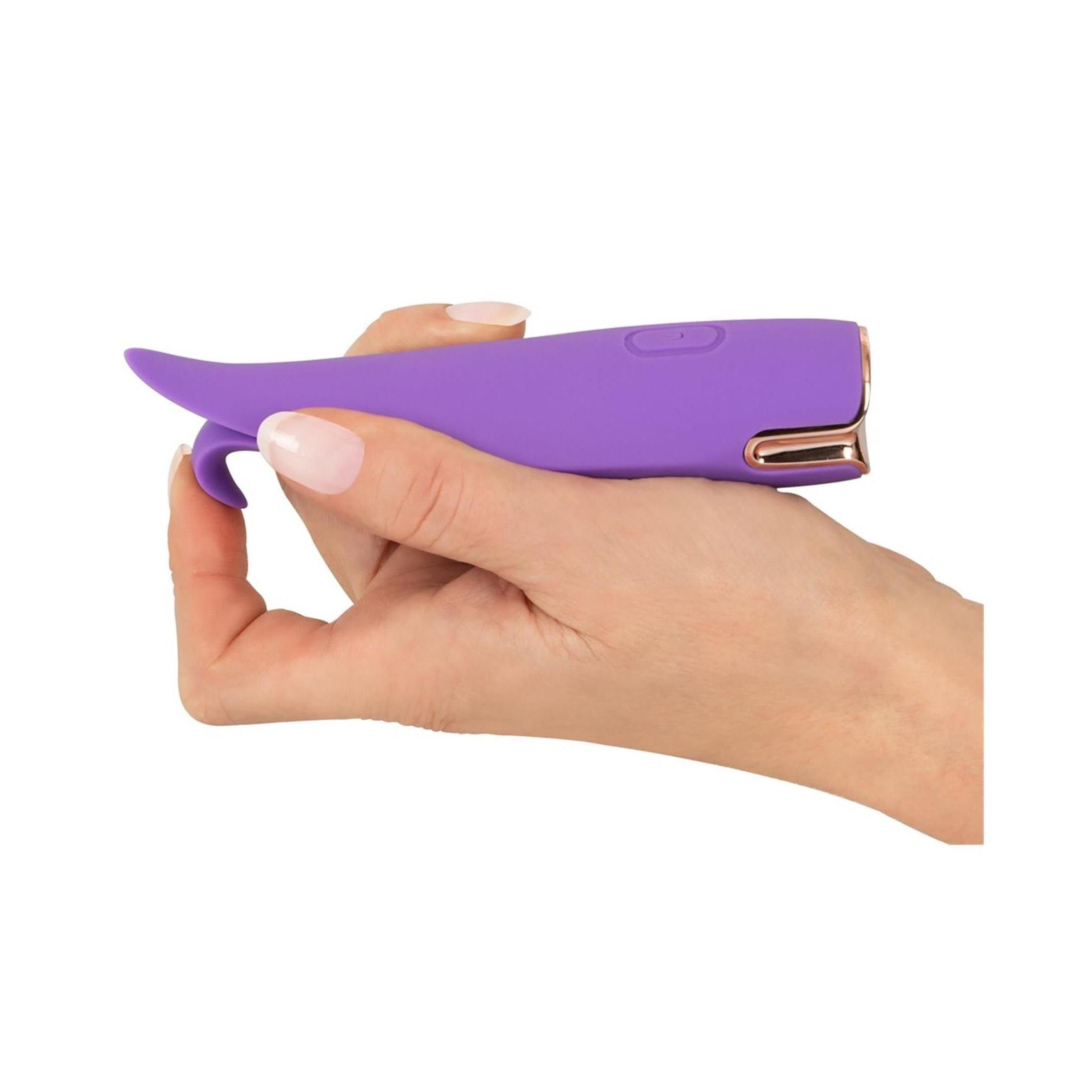 Mano che tiene uno stimolatore viola. Dettagli dorati. Un pulsante. Forma a due petali.