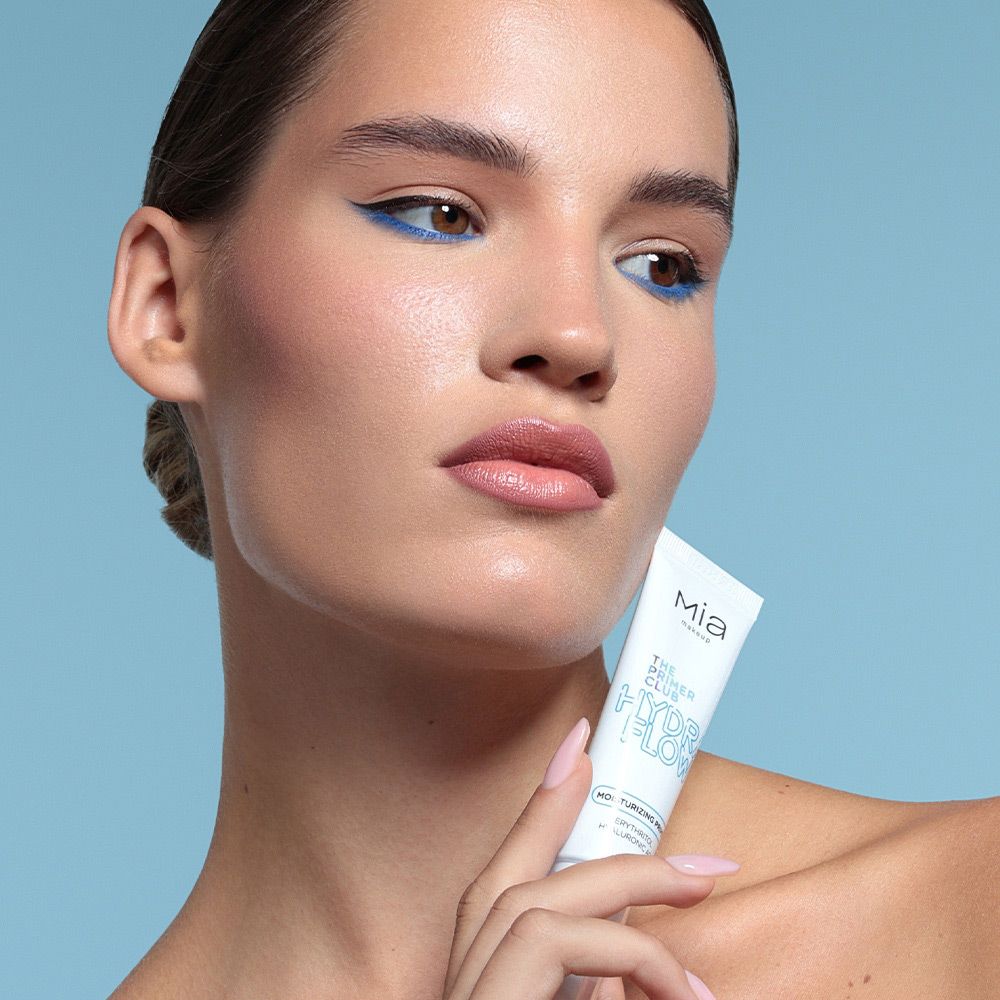 Una donna tiene un tubo di Mia Makeup Hydra Flow Primer. Il tubo è bianco con testo blu. La donna ha un trucco occhi blu.