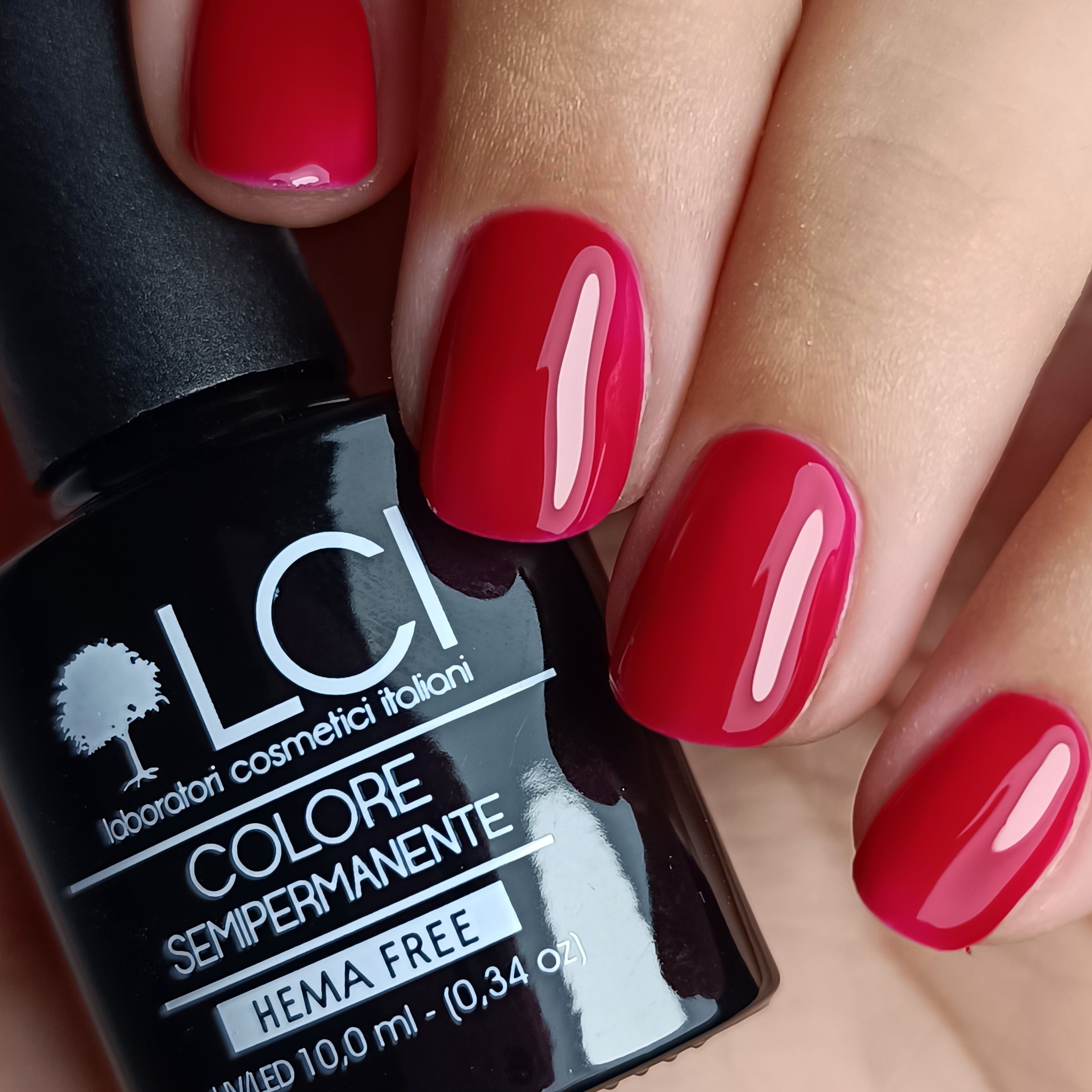 Mano con unghie rosse smaltate e flacone di smalto. Scritta: LCI, Colore Semipermanente, HEMA FREE.