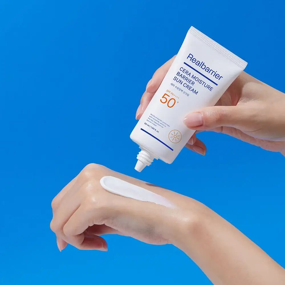 Tubo bianco con crema solare Realbarrier. Crema applicata sulla mano. Scritta: Cera Moisture Barrier Sun Cream SPF 50. Crema chiara.