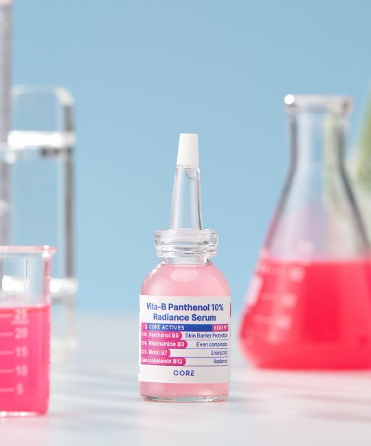 Flacone trasparente con liquido rosa, davanti a vetreria da laboratorio. Etichetta con nome e ingredienti. Applicatore bianco.