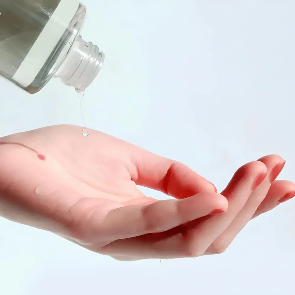 Mano con smalto rosso che riceve liquido da un flacone. Il liquido gocciola sul palmo.