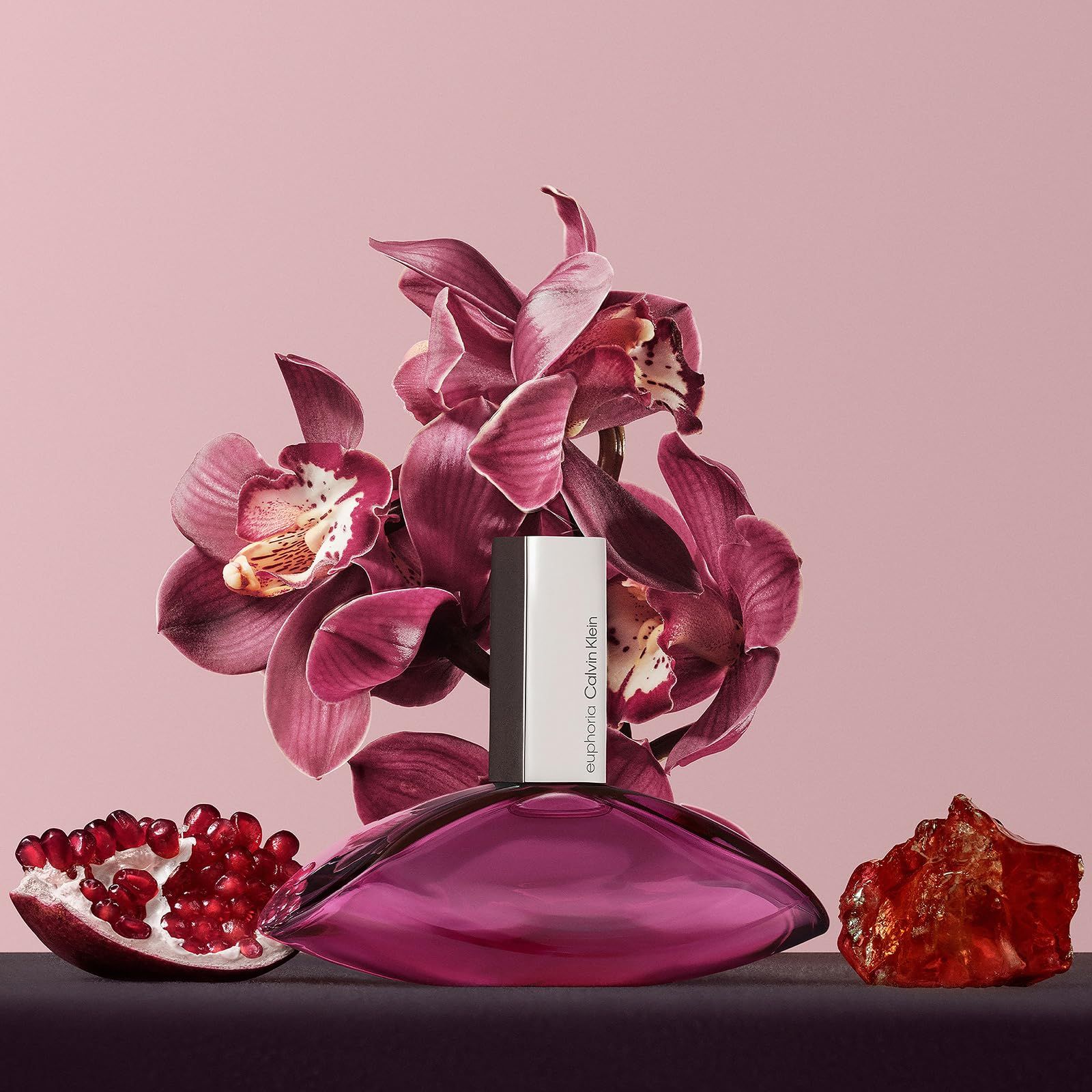 Flacone di profumo con fiori e melograno. Flacone a goccia, argentato. Fiori e melograno in scena.