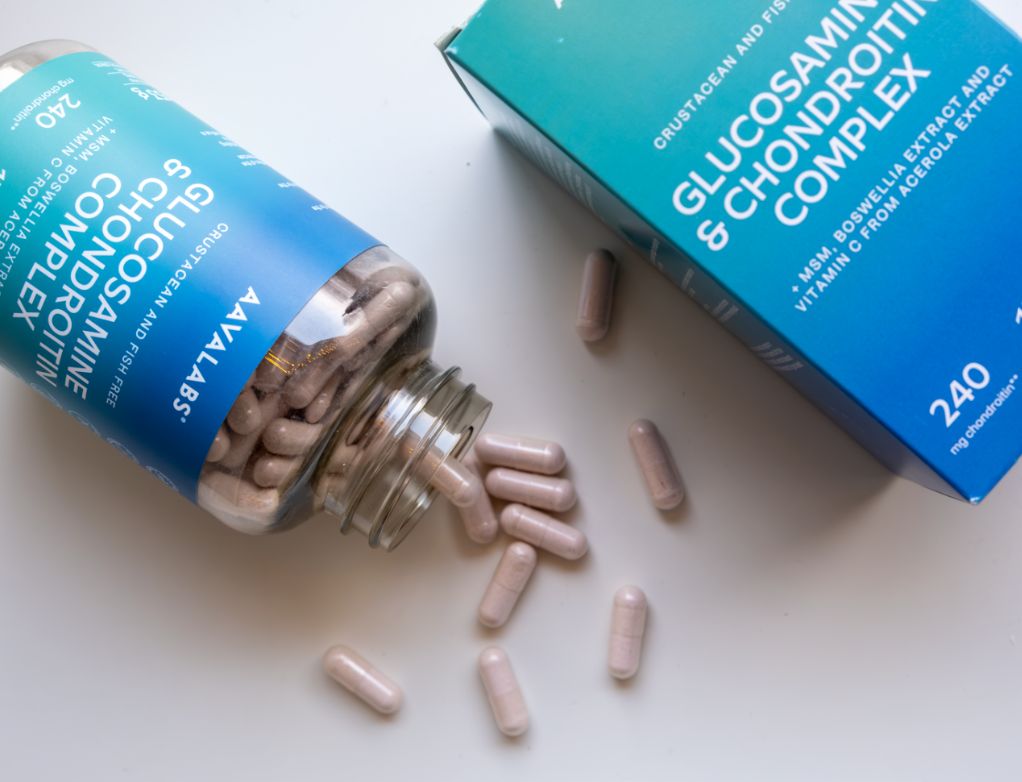 Capsule di glucosamina rovesciate da una bottiglia su una superficie.