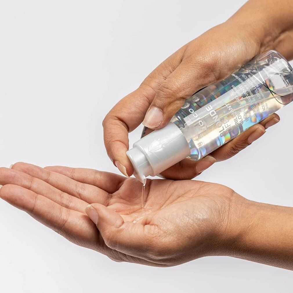 Mani che tengono una bottiglia di olio per capelli, versando l'olio sul palmo. Olio trasparente visibile.