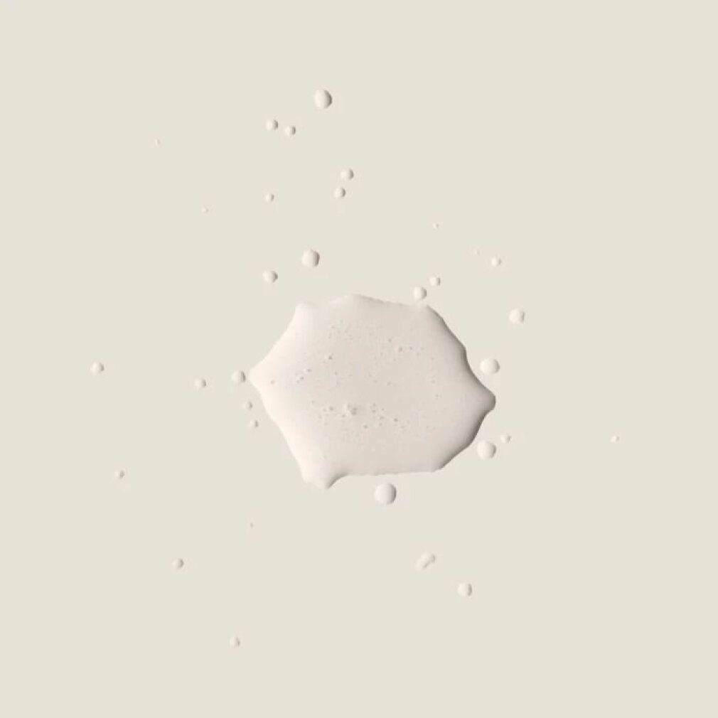 Liquido chiaro con gocce su sfondo beige. Forma geometrica. Nessuna informazione sul prodotto visibile.