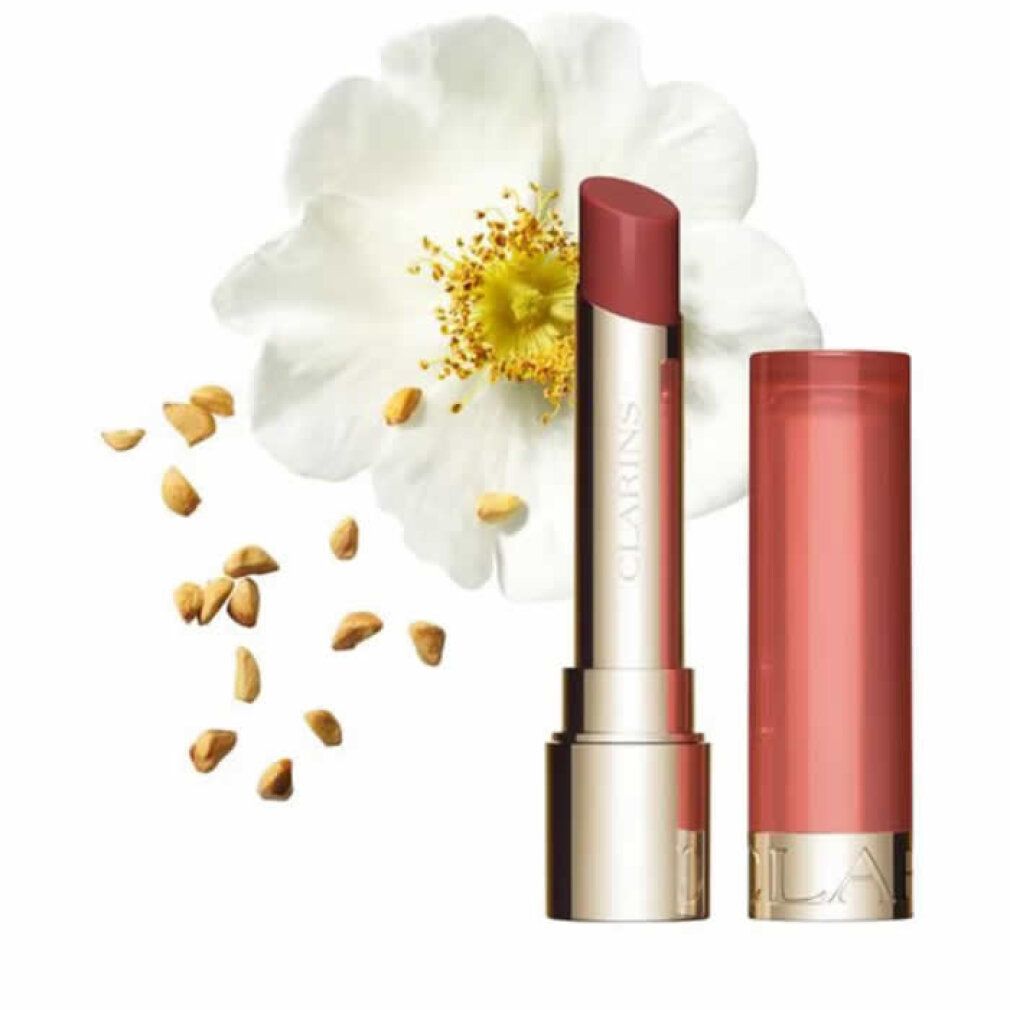 Balsamo per labbra accanto a fiore e semi. Contenitore dorato con rossetto rosa. Marchio Clarins visibile.
