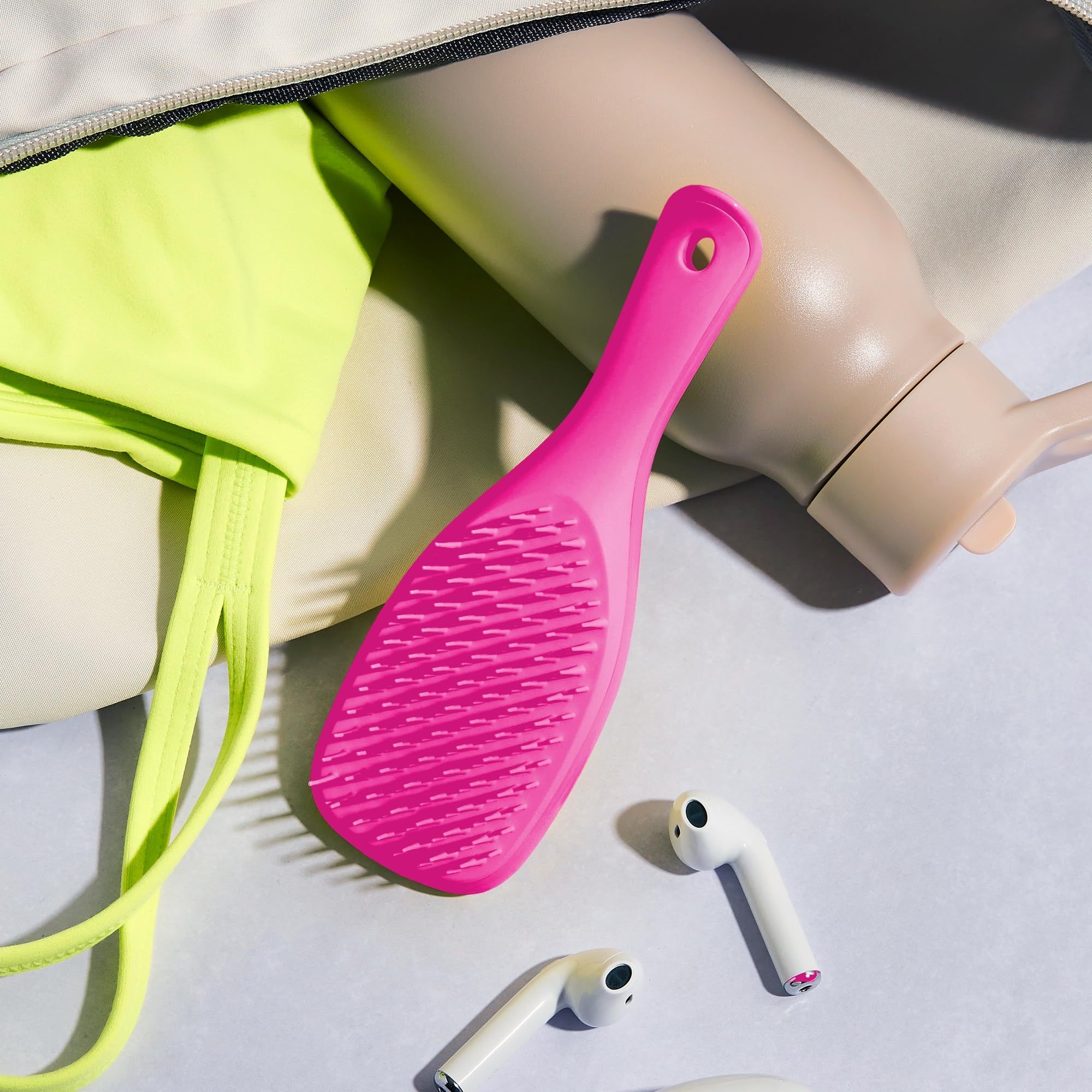 Spazzola rosa in una borsa, accanto a abbigliamento sportivo, borraccia e auricolari.