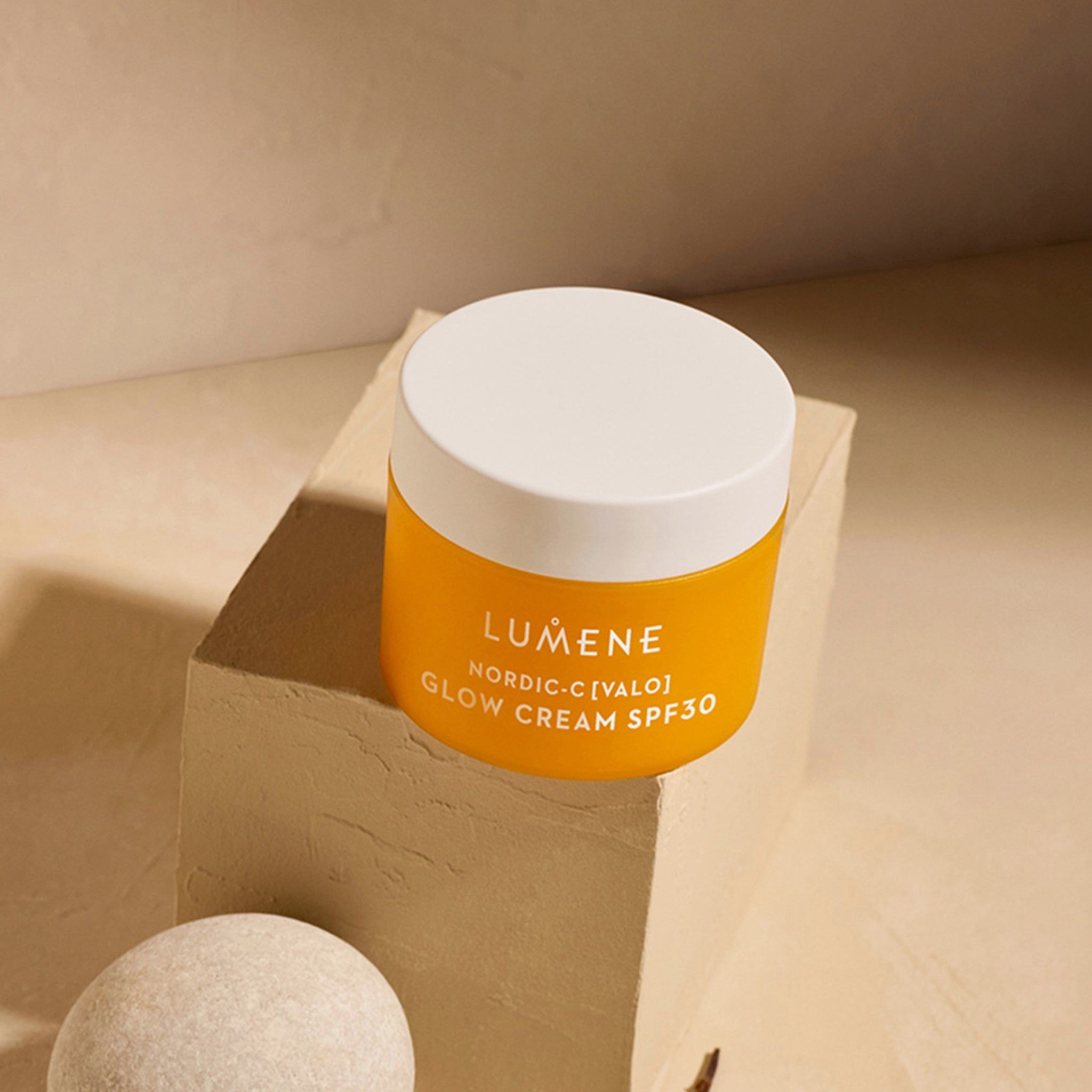 Vasetto di crema giallo con coperchio bianco su un piedistallo. Scritta: LUMENE, NORDIC-C [VALO] GLOW CREAM SPF30.