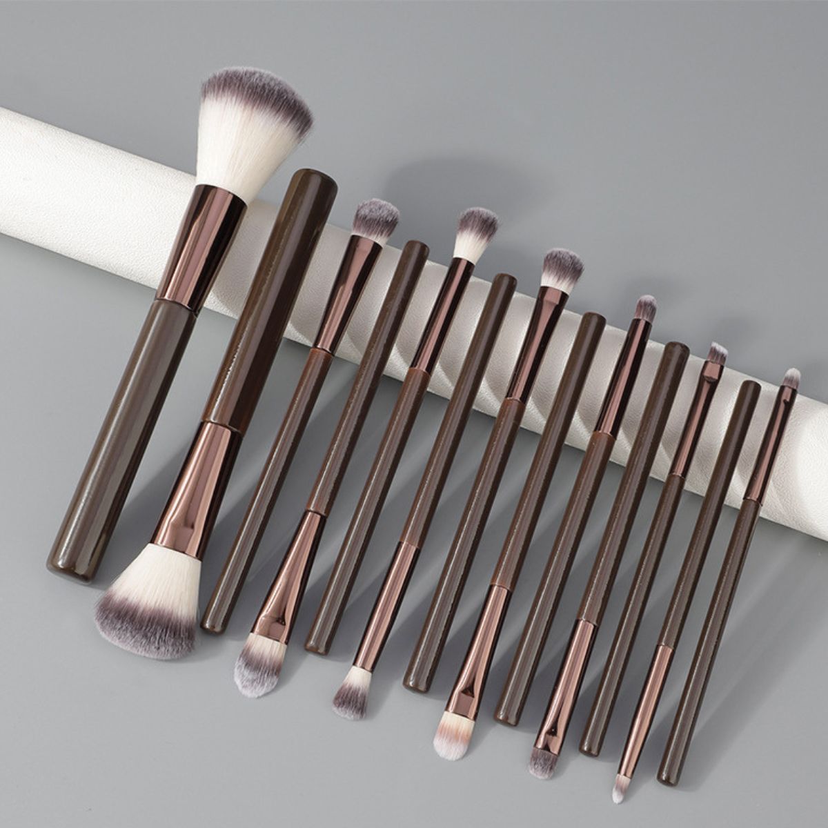 Un set di 12 pennelli per il trucco scuri con accenti oro rosa e setole morbide.