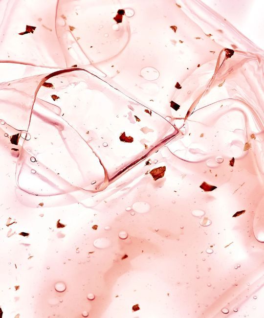 Primo piano di idrogel rosa con particelle scure e goccioline d'acqua. Struttura ondulata.