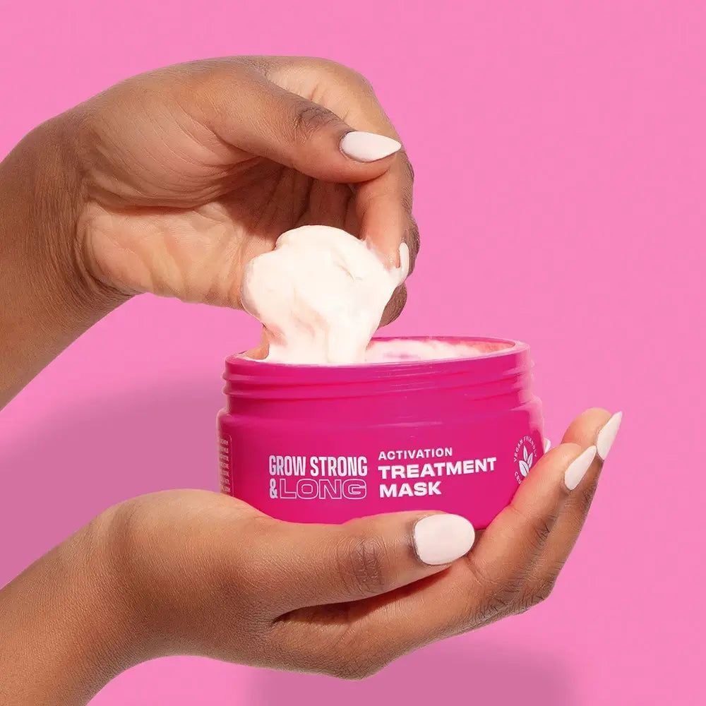 Mani prelevano una maschera cremosa da un vasetto rosa 'Grow Strong & Long'.