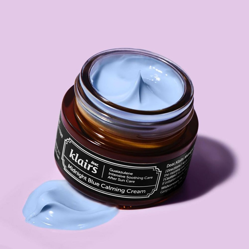 Vasetto di crema aperto, crema blu visibile. Nome del prodotto e marchio sull'etichetta. Macchia di crema accanto.