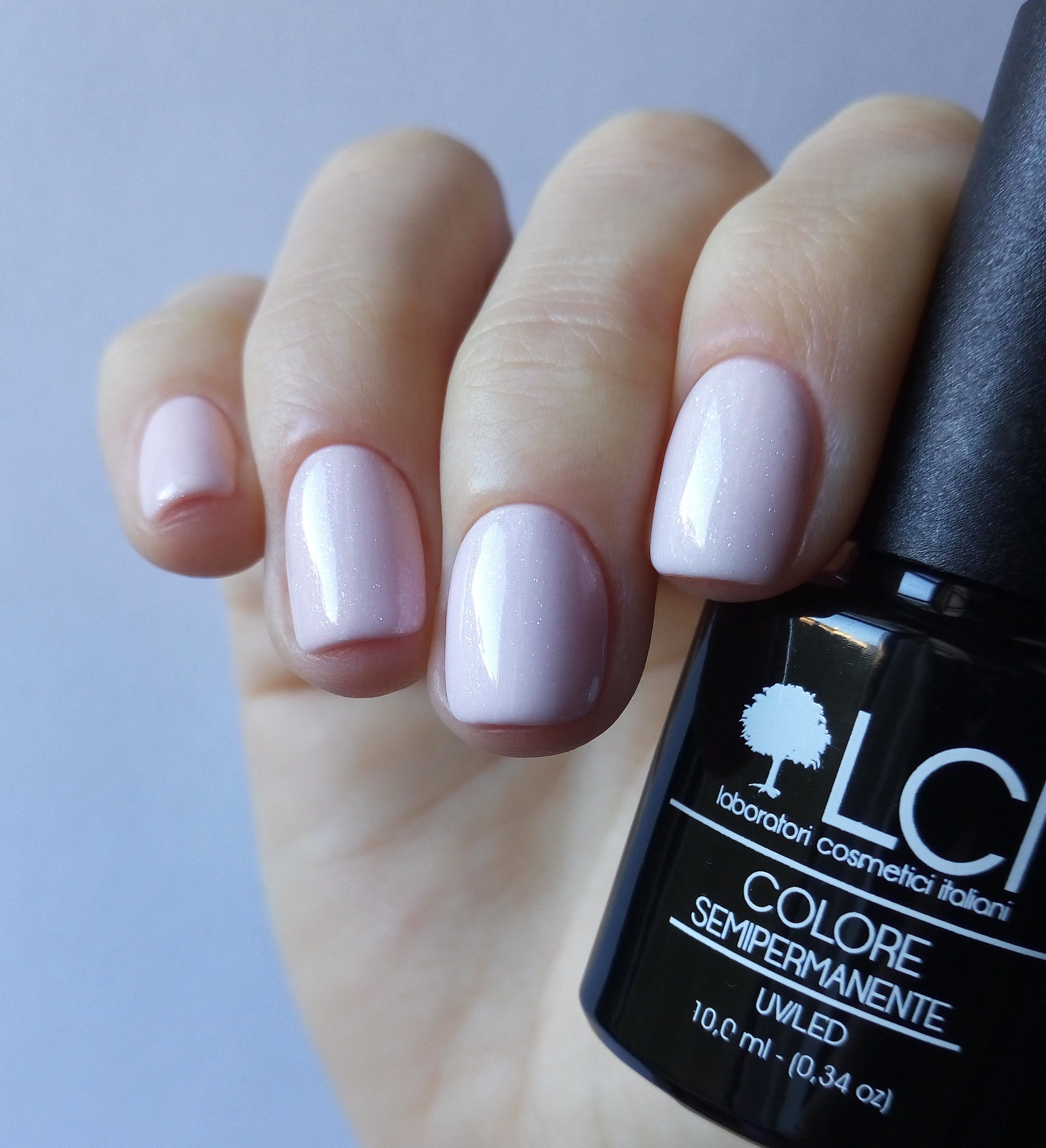 Mano con unghie smaltate e flacone di smalto. Rosa. Scritta: LCI, COLORE SEMIPERMANENTE, UVLED, 10,0 ml.