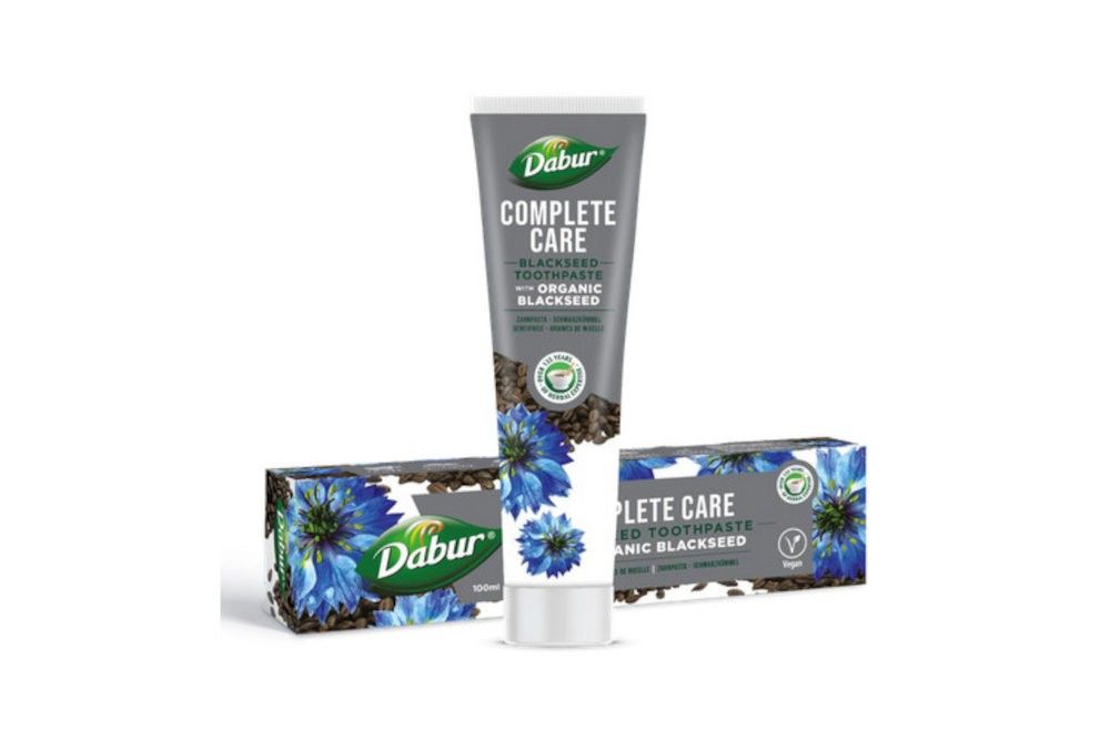Tubo e due scatole di dentifricio Dabur Complete Care Nigella con motivo fiordaliso.
