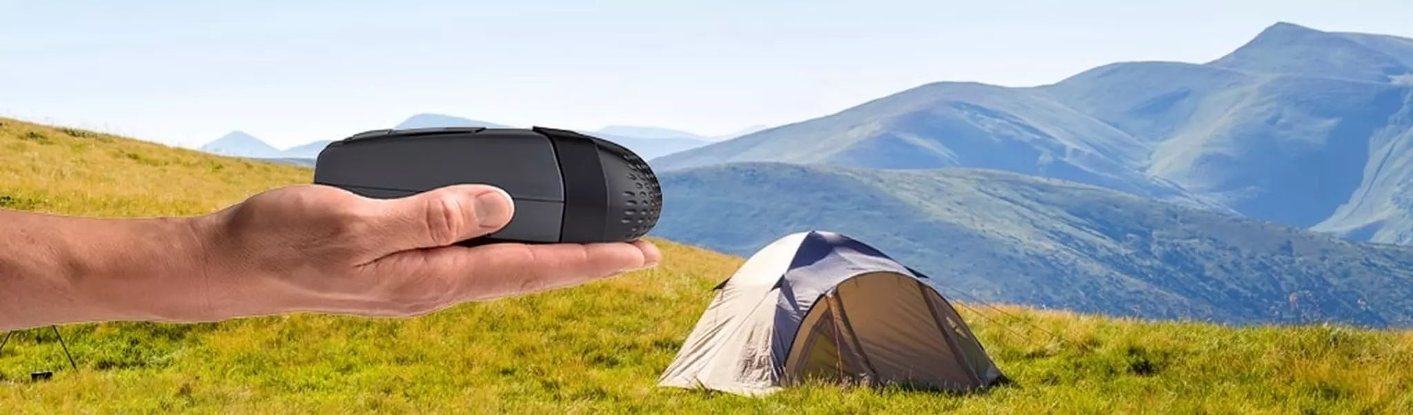 Dispositivo CPAP da viaggio grigio compatto in una mano, davanti a un paesaggio montano e una tenda.